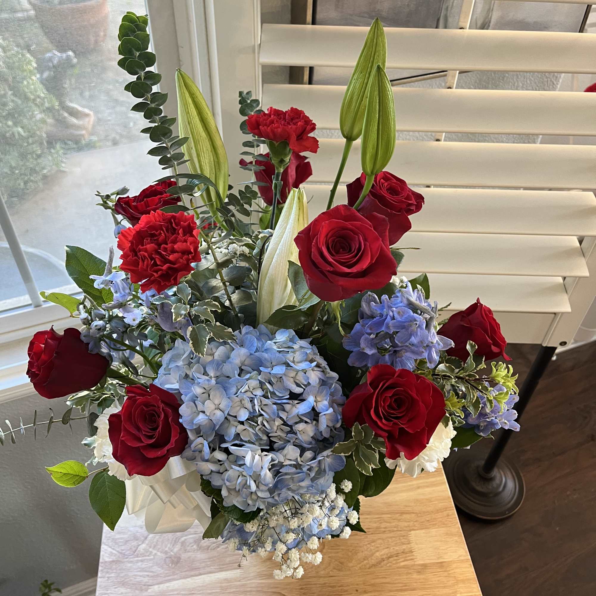 Bouquet of red roses, blue hydrangea, and lilies in a white wrap