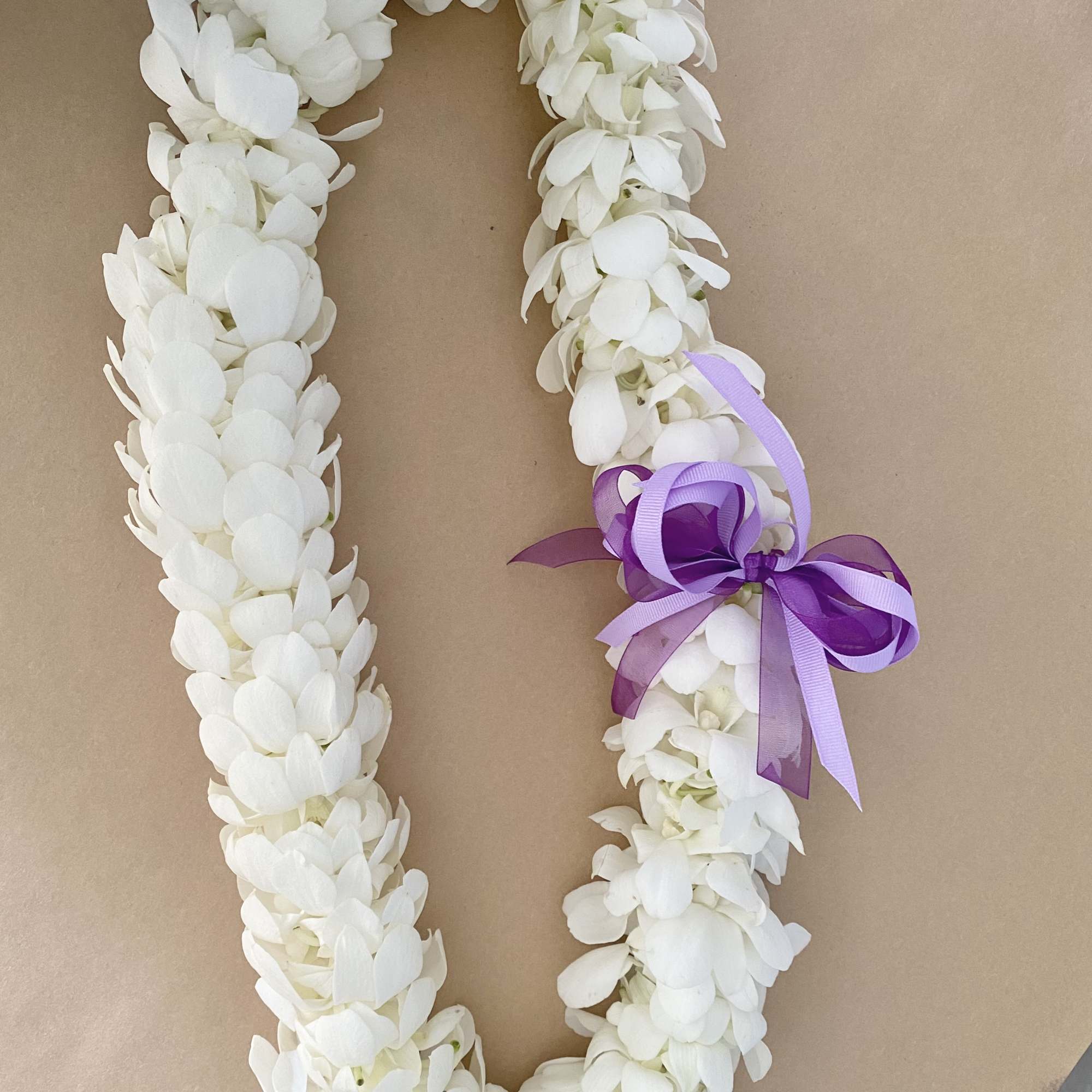 White flower lei with a purple ribbon bow on brown paper