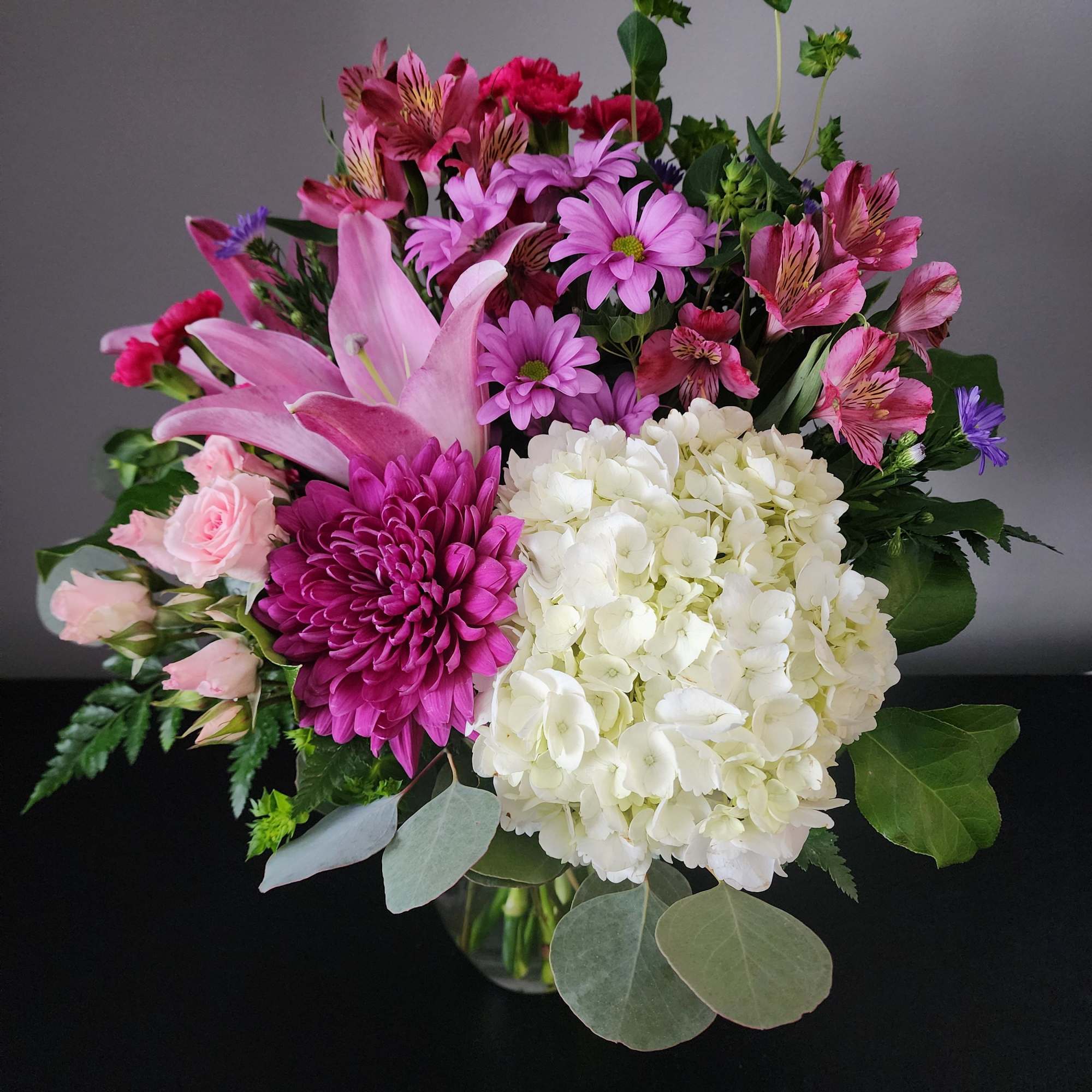 Mixed bouquet with pink lilies, white hydrangea, and magenta chrysanthemums in a glass vase
