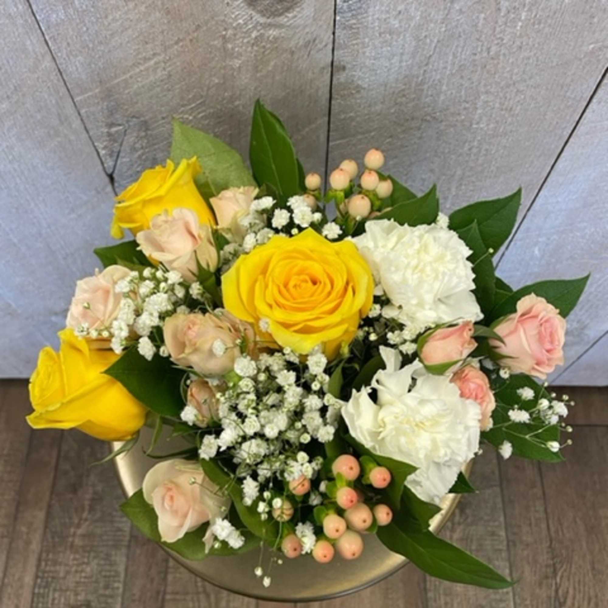 Bouquet of yellow and blush roses with white blooms in a round container