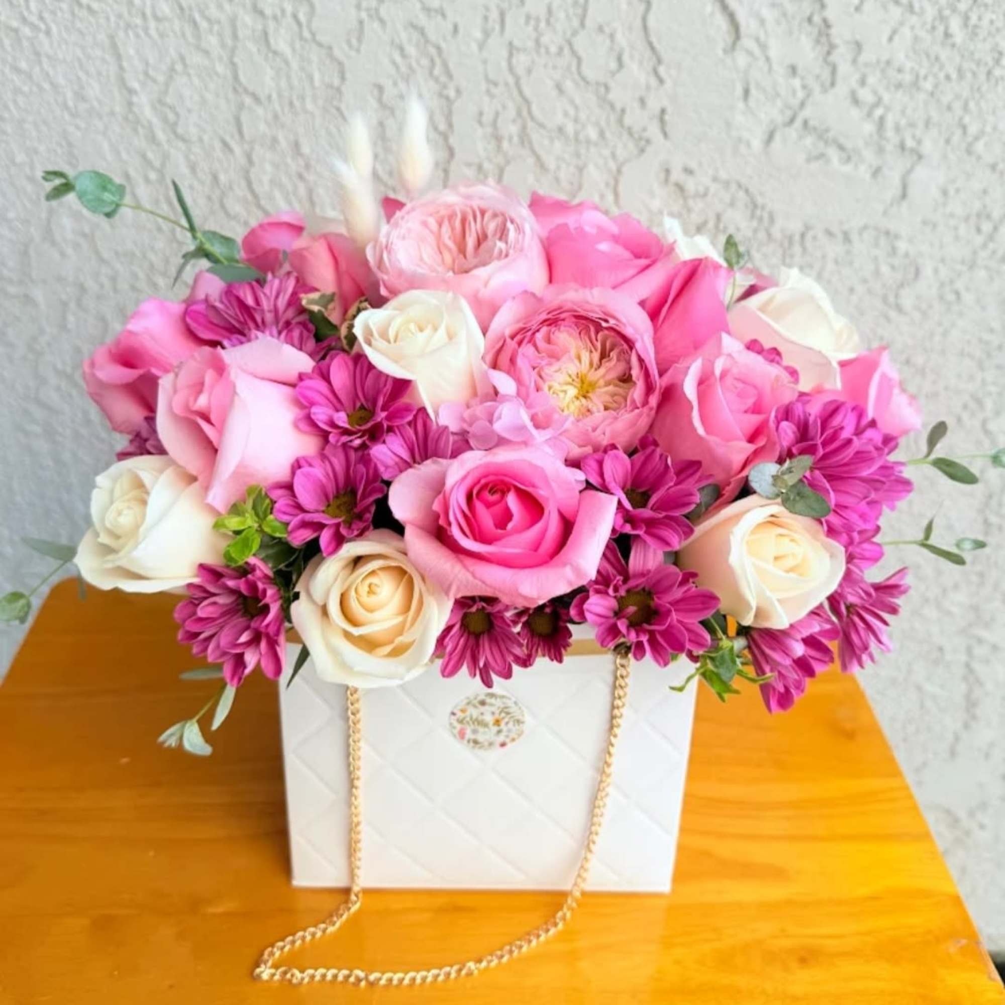 Pink and white roses with magenta daisies in a white gift bag
