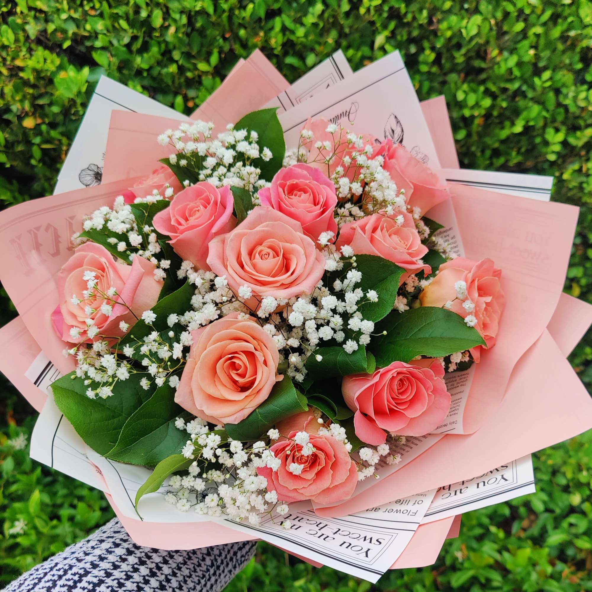 Hand-tied bouquet of peach roses and white filler flowers wrapped in pink paper