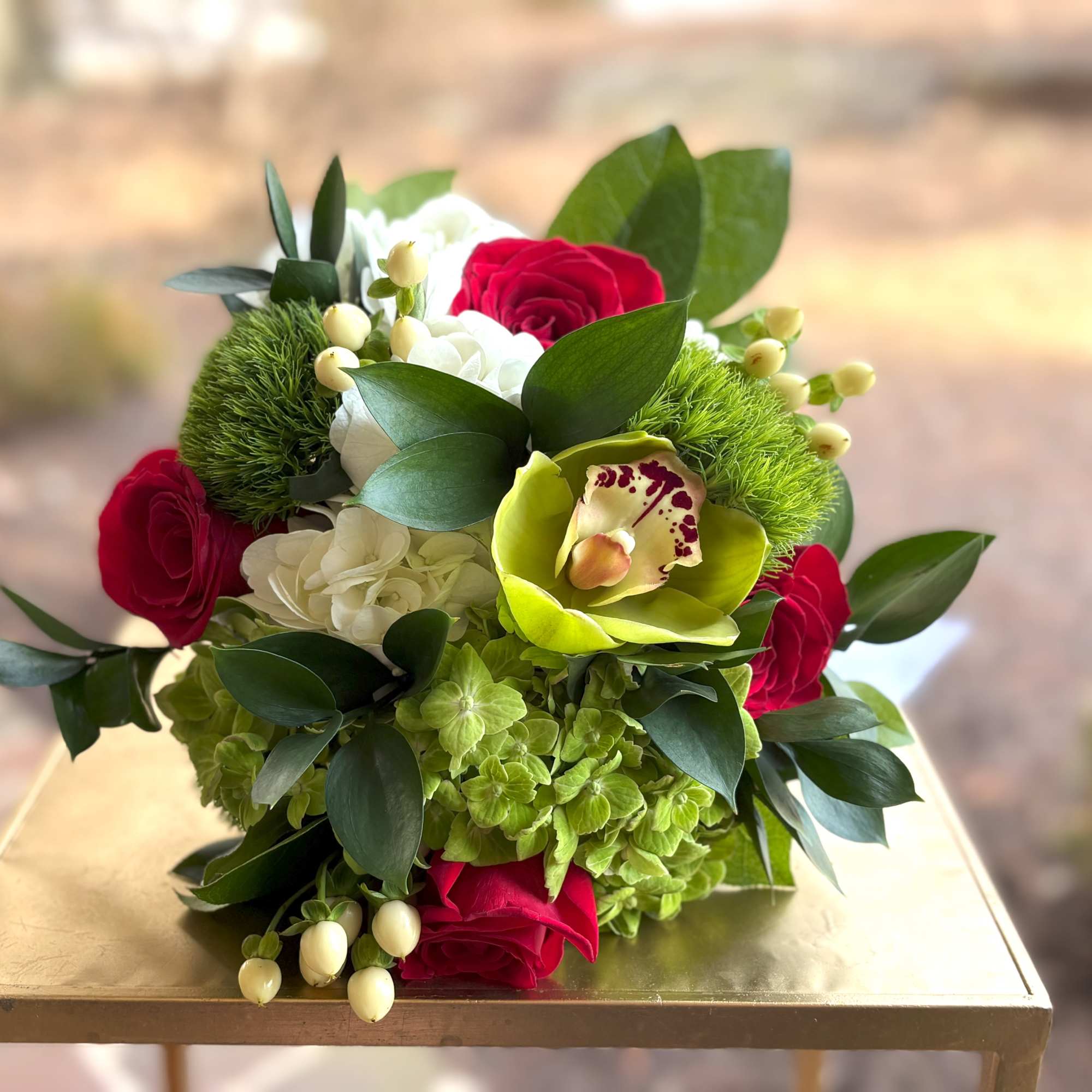 Low arrangement of red roses, green hydrangeas and a green cymbidium orchid in a compact design