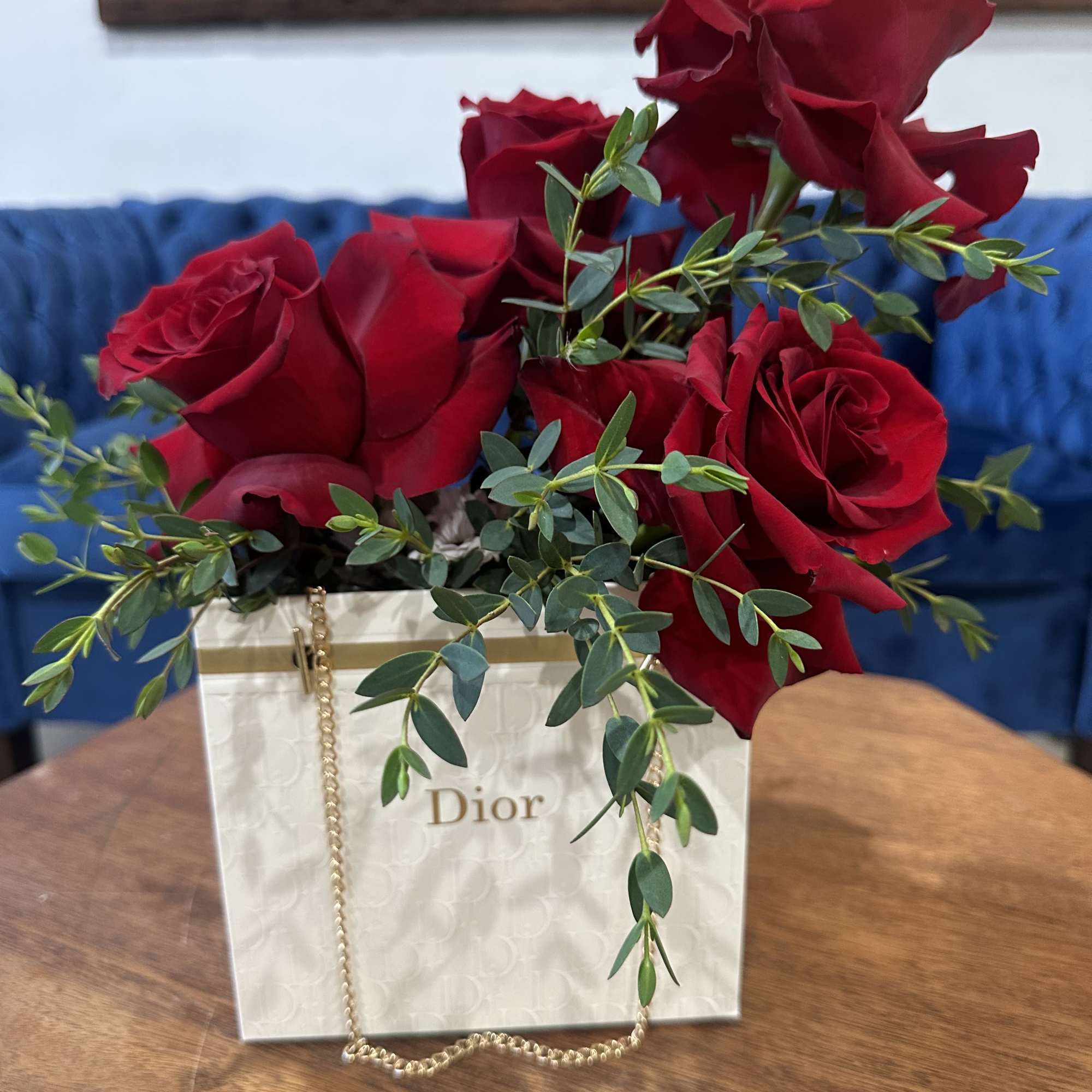 Red roses arranged in a white Dior gift bag with greenery.