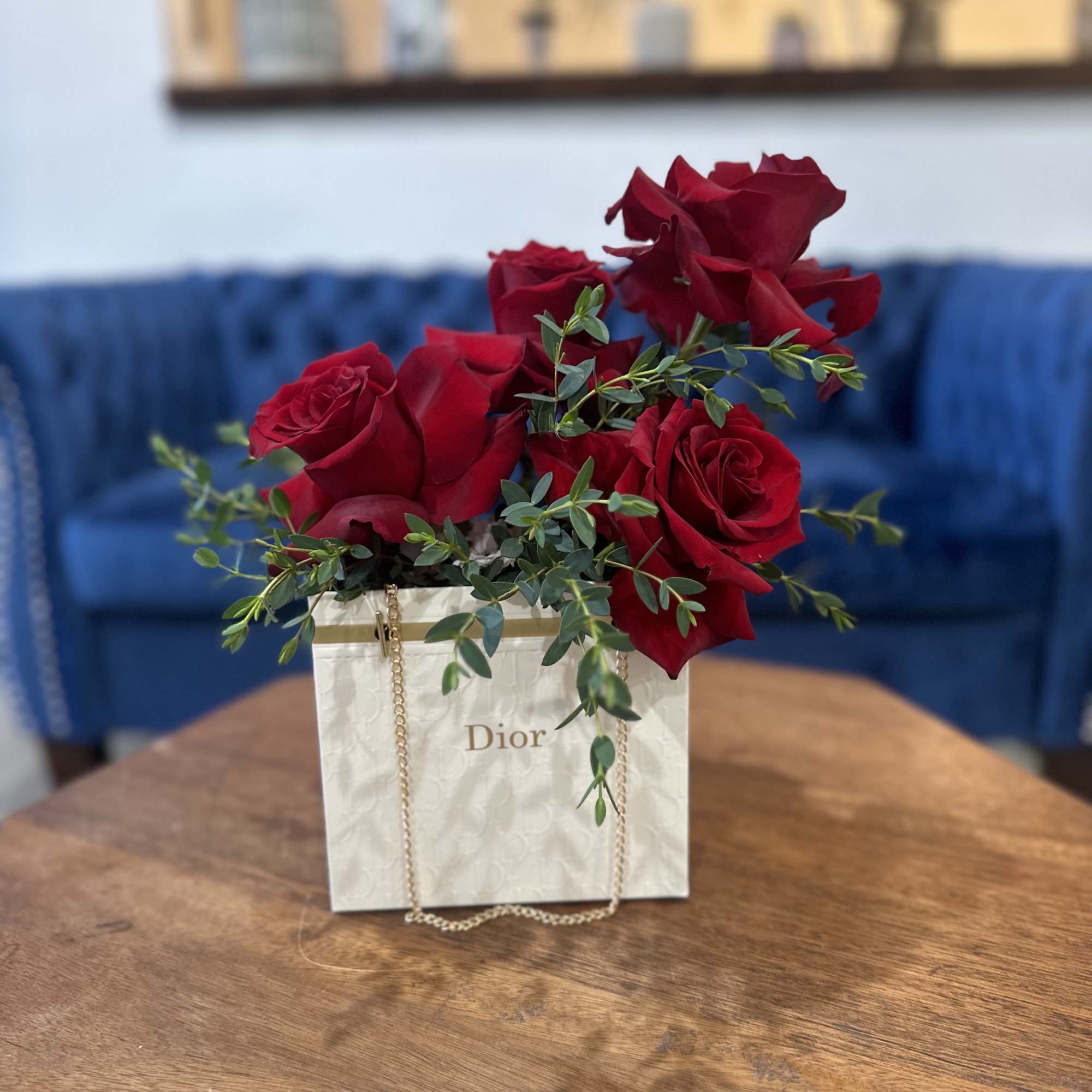Red roses arranged in a Dior gift bag on a table