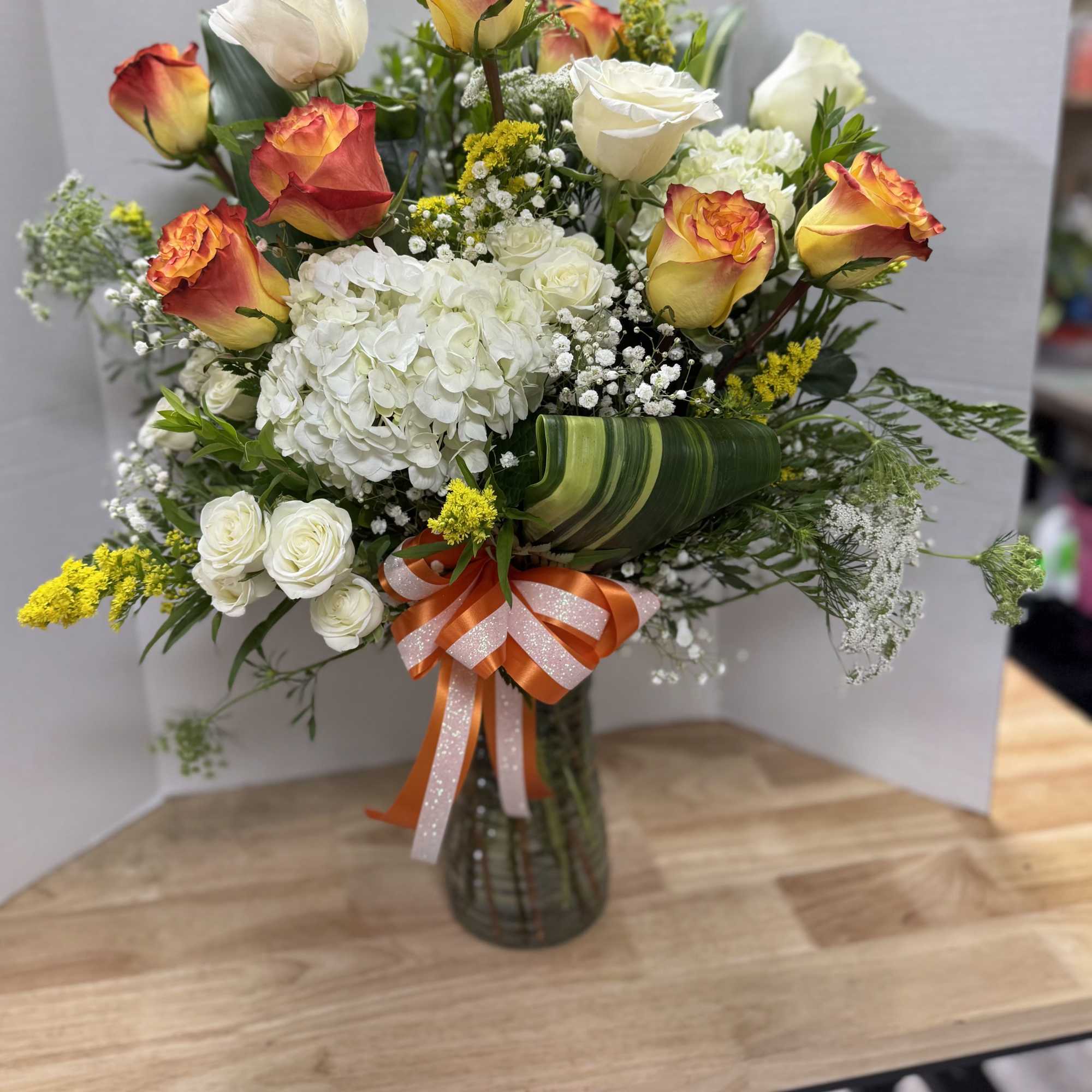 Bouquet of orange-tipped roses, white hydrangea, and baby's breath in a glass vase