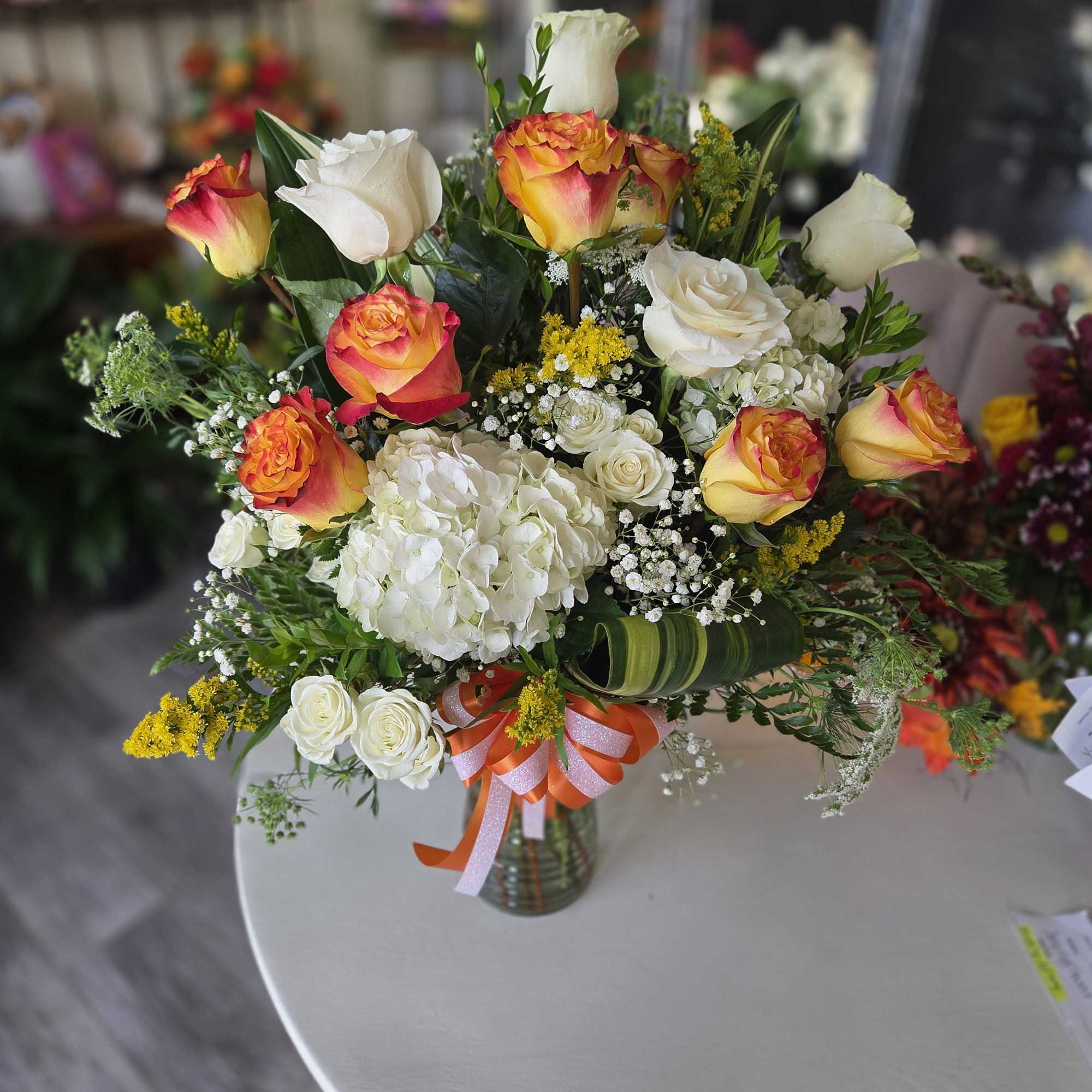 Bouquet of orange-and-yellow roses with white hydrangea in a glass vase