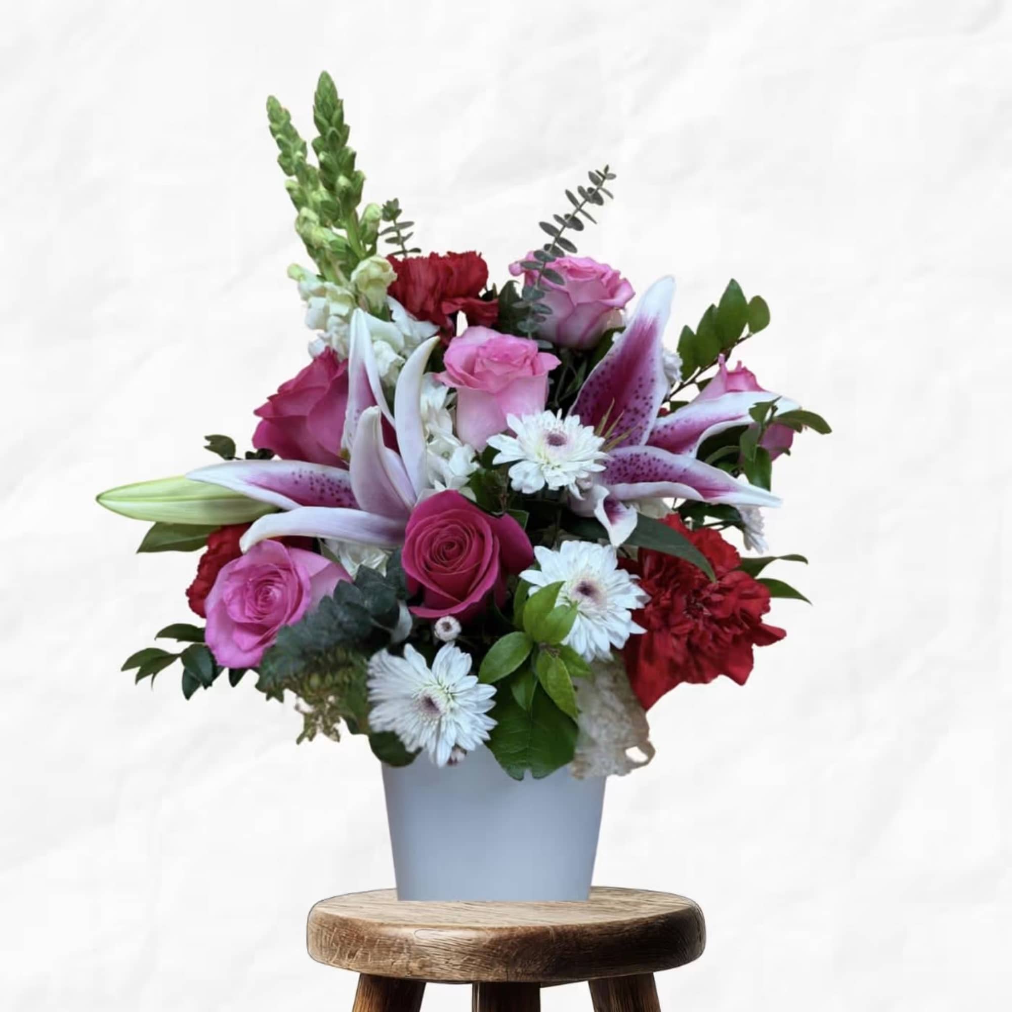 Mixed bouquet of pink roses, lilies, and white daisies in a blue vase