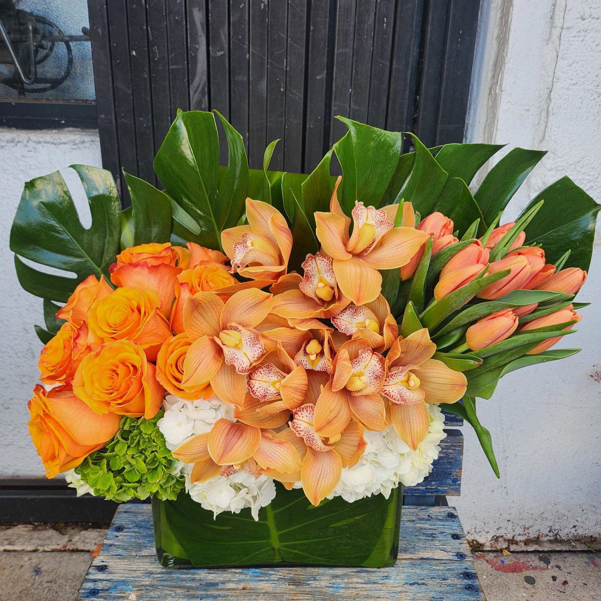 Orange roses and orchids in a glass vase with tropical leaves