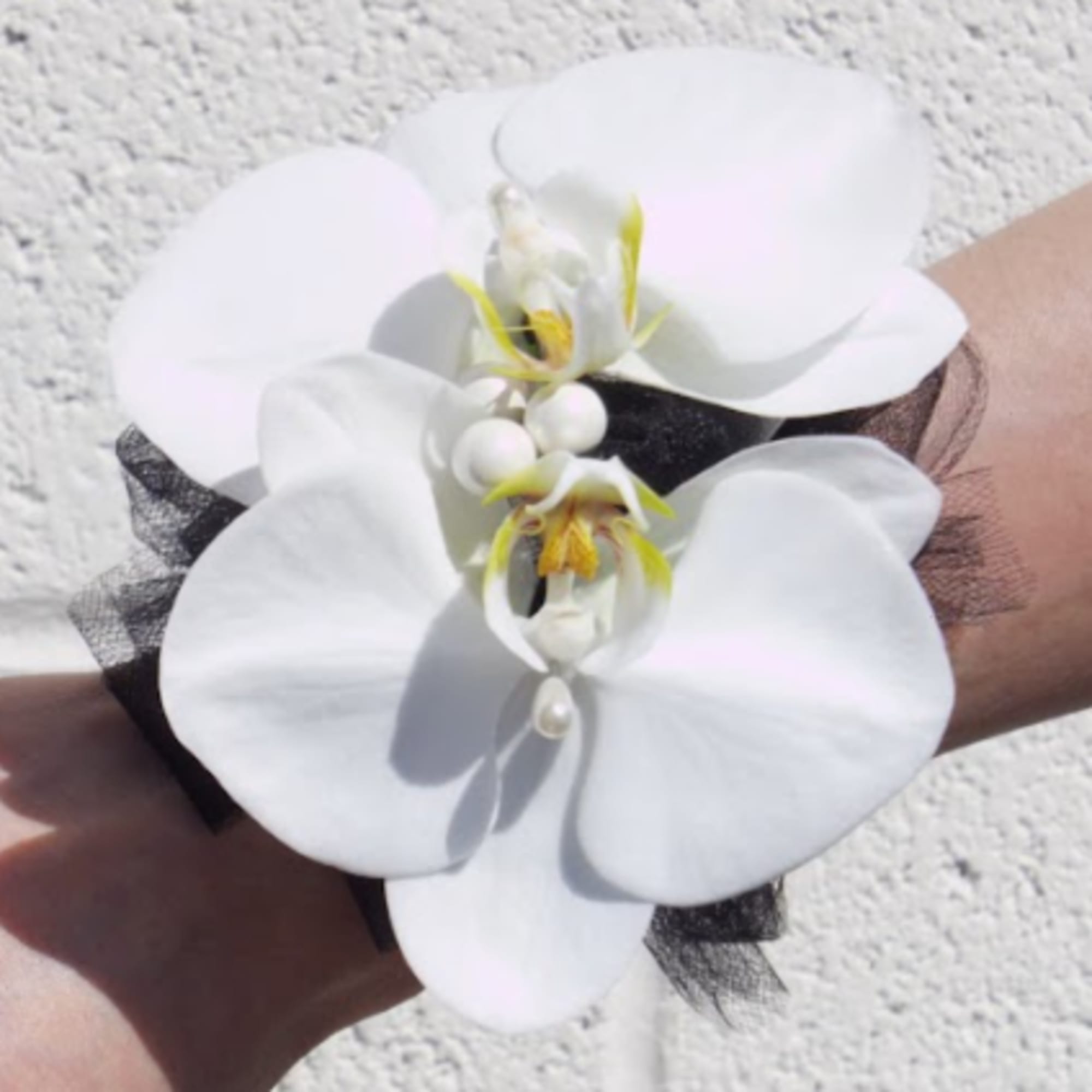 White orchid wrist corsage with black ribbon and pearl accents