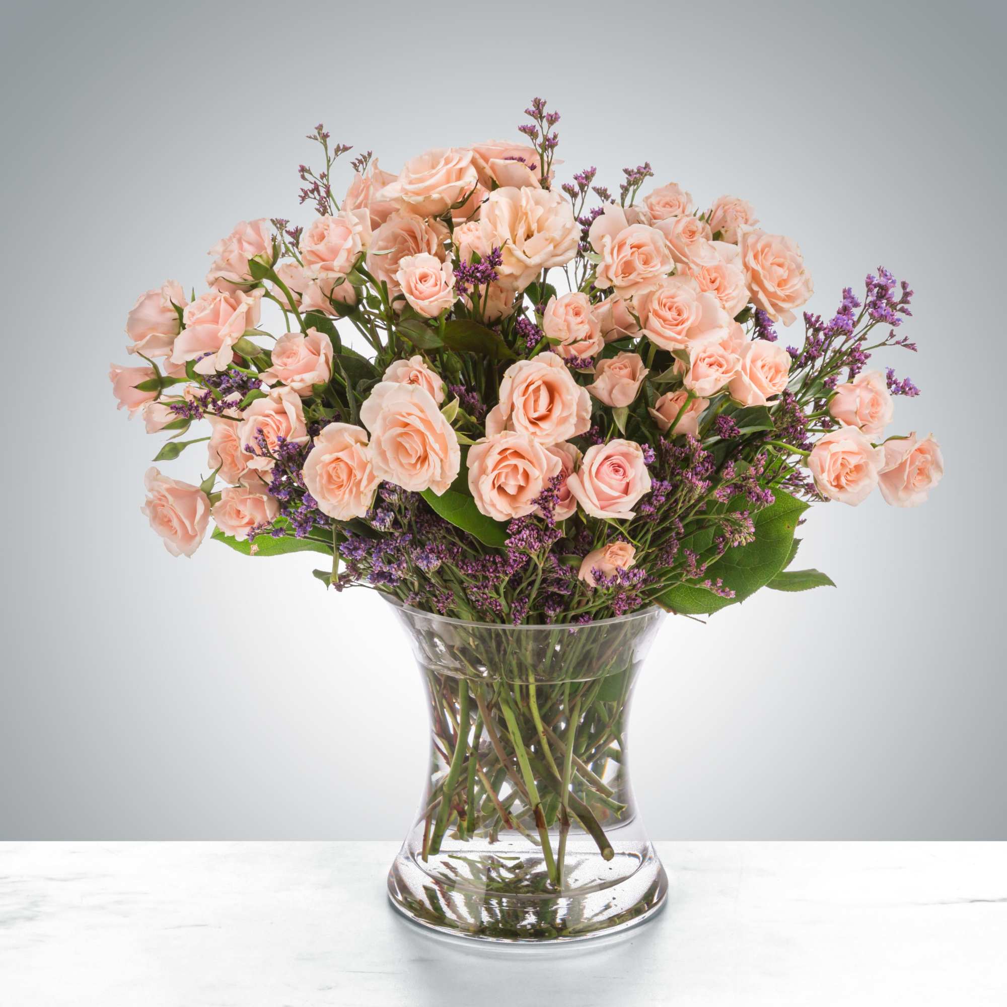 Peach roses arranged in a clear glass vase with purple filler flowers