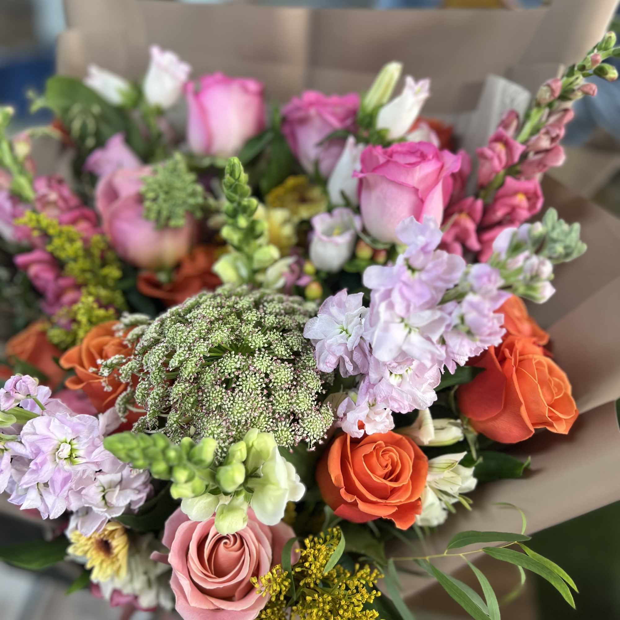 Mixed bouquet of pink, orange, and lavender flowers wrapped in brown paper