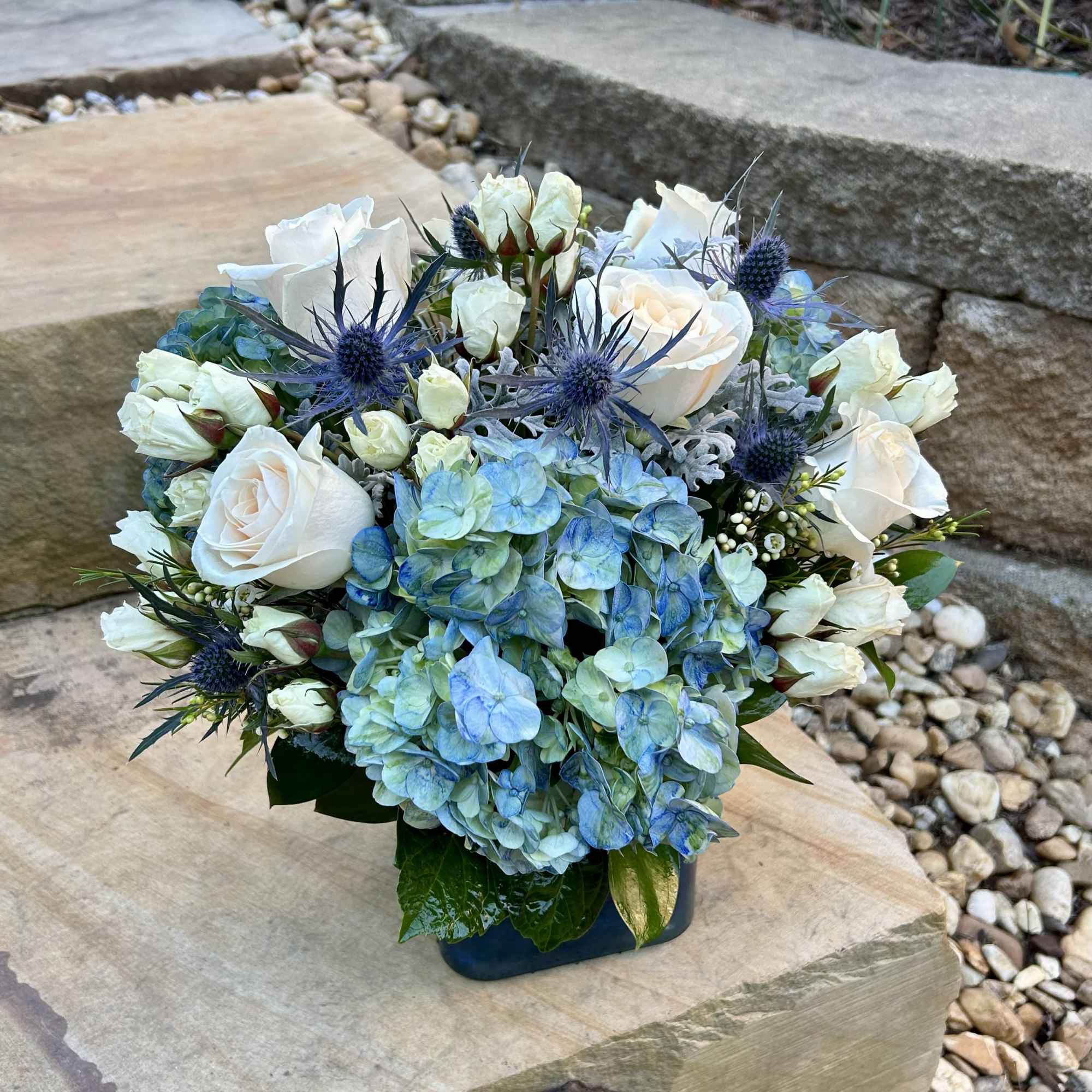 Blue hydrangea and white rose arrangement in a dark vase