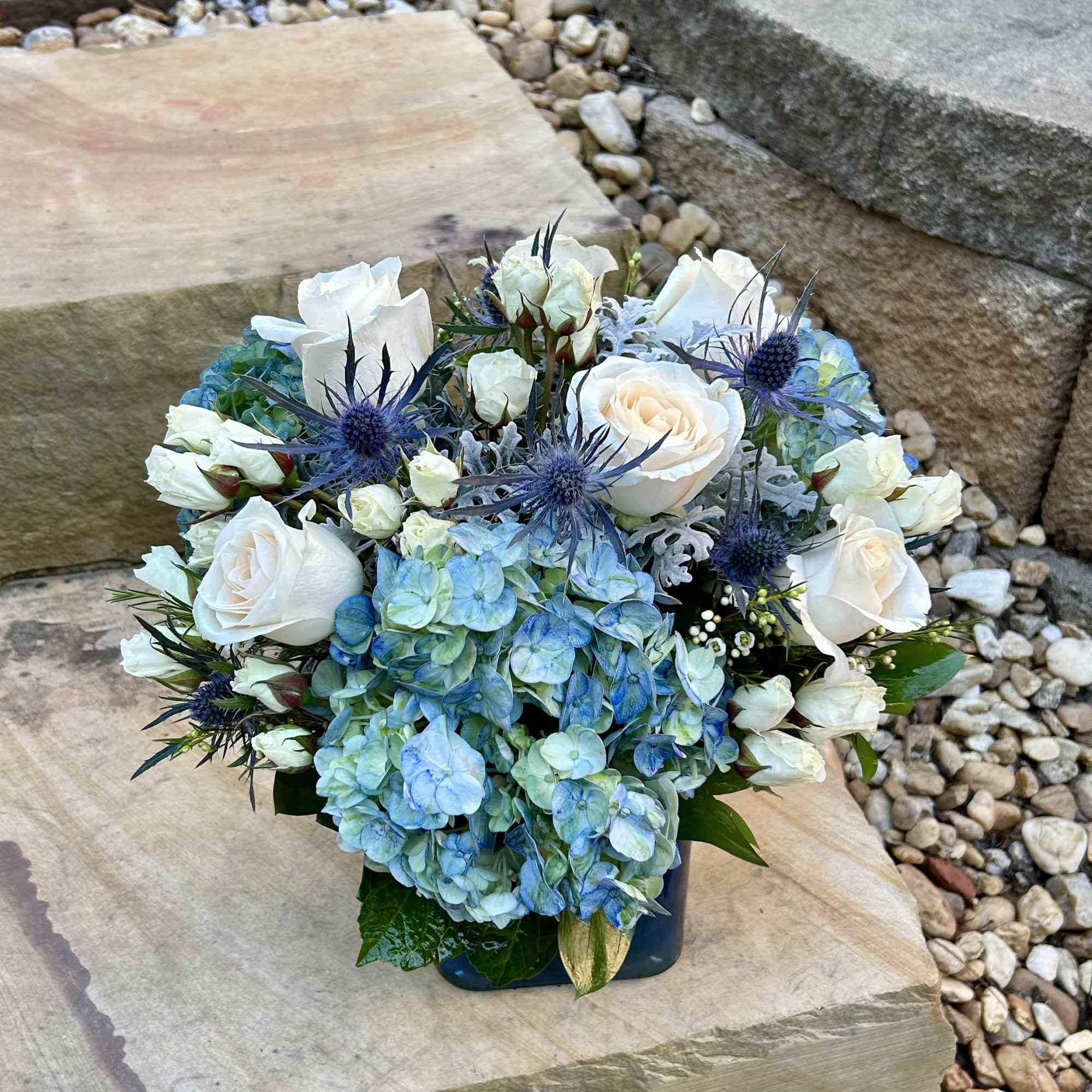 Blue hydrangeas and white roses arranged in a low square vase
