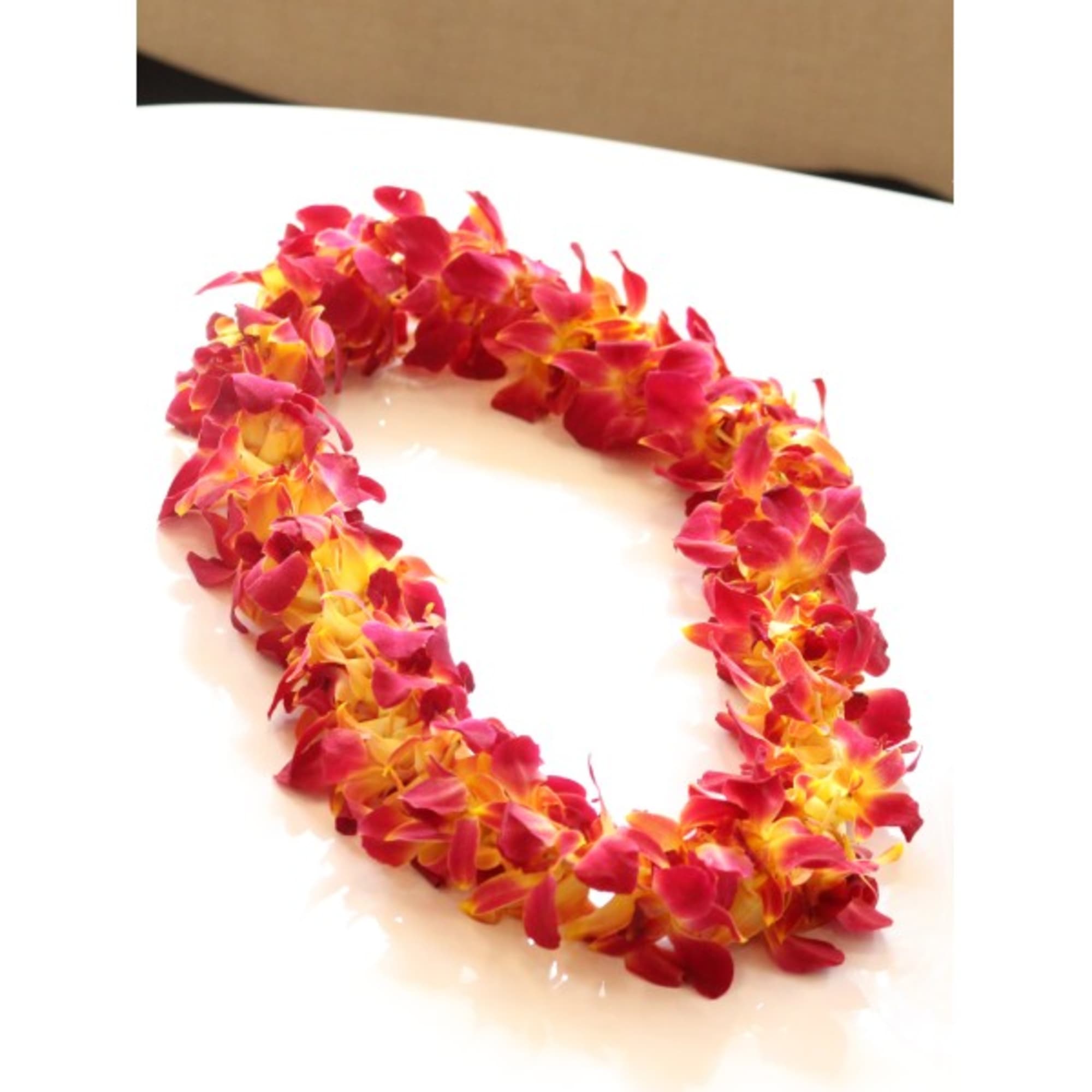 Pink and yellow flower lei on a white surface