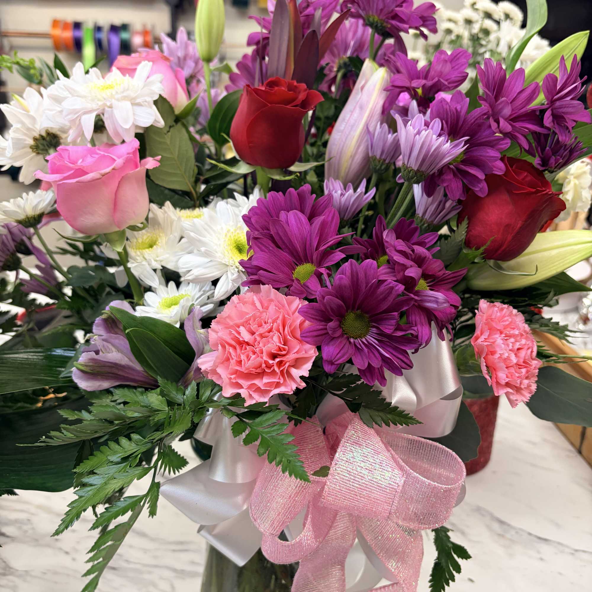 Mixed bouquet of roses, daisies, lilies, and carnations in a glass vase