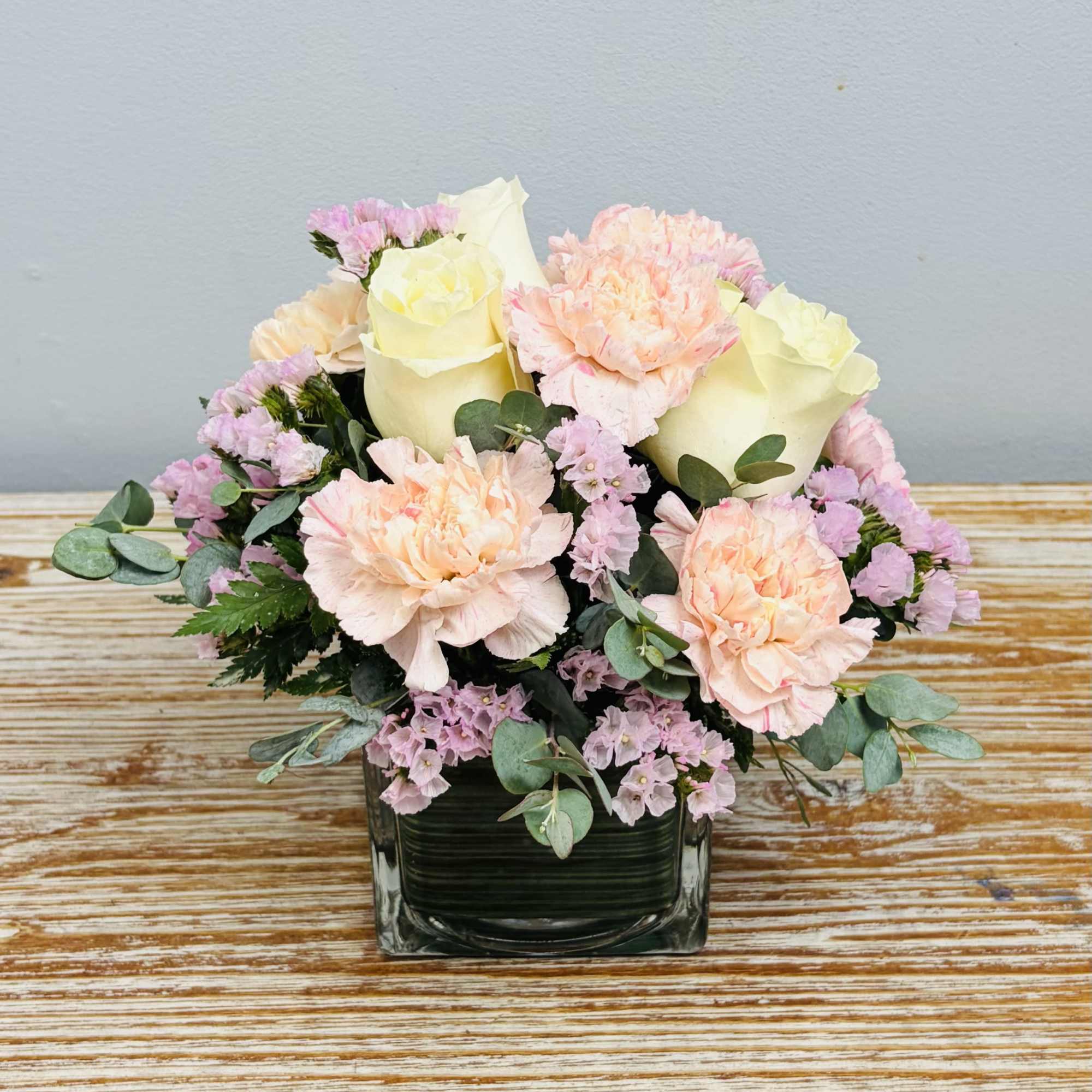 Shades of pink and white blooms arranged in leaf wrapped glass cube