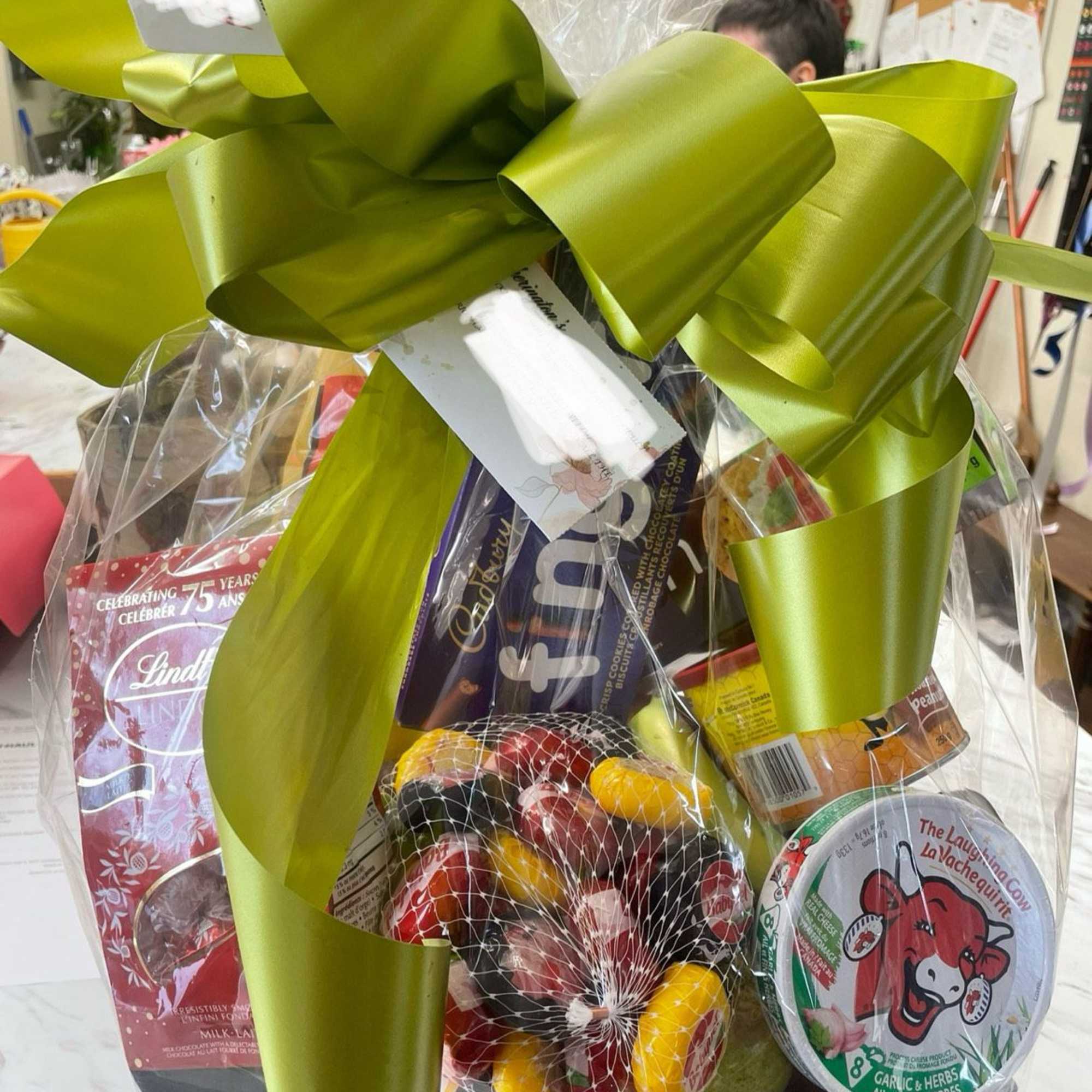 Gift basket with chocolates, candy, and cheese wrapped in clear cellophane with a large green bow
