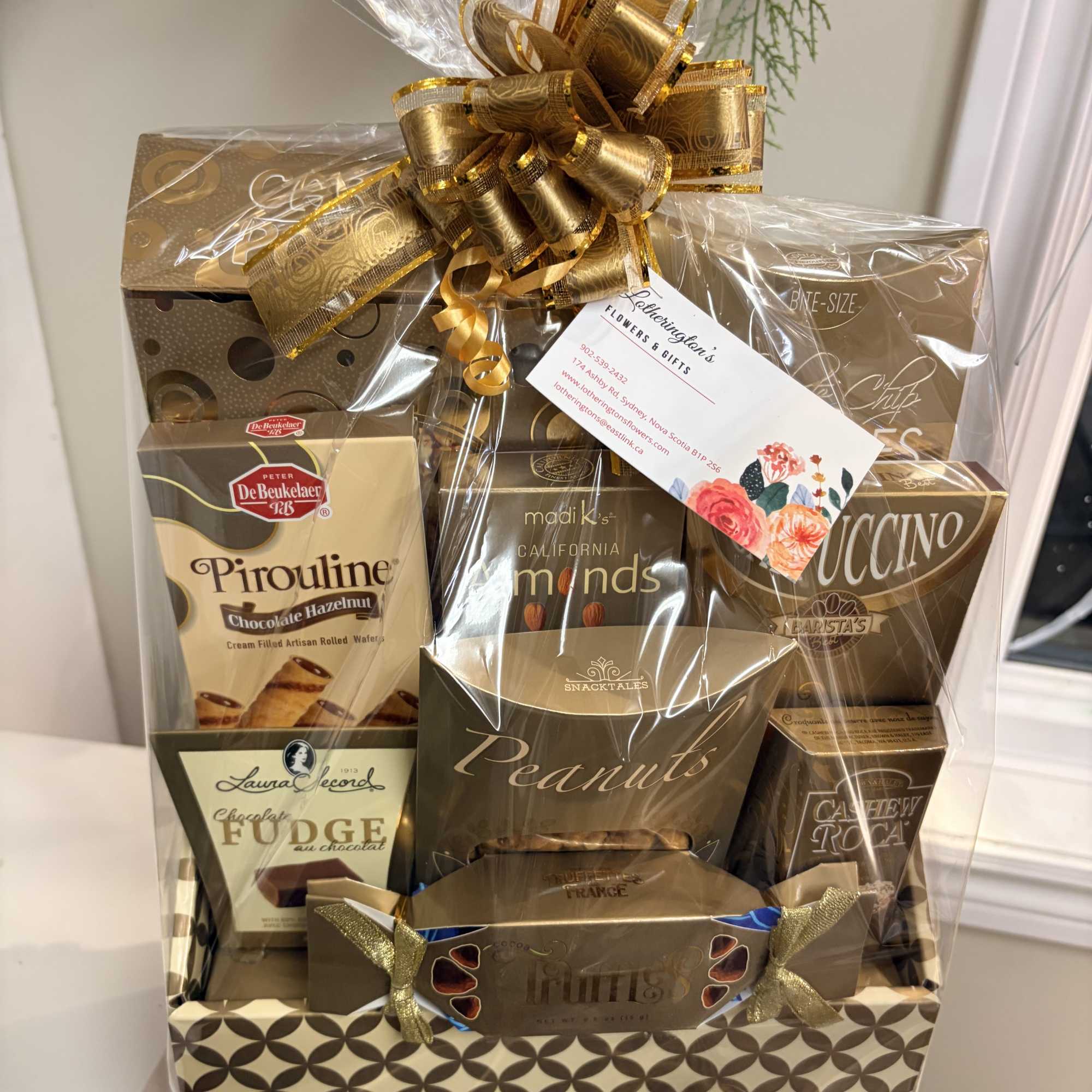 Gold-toned gourmet snack and chocolate gift basket wrapped in cellophane with a large gold bow