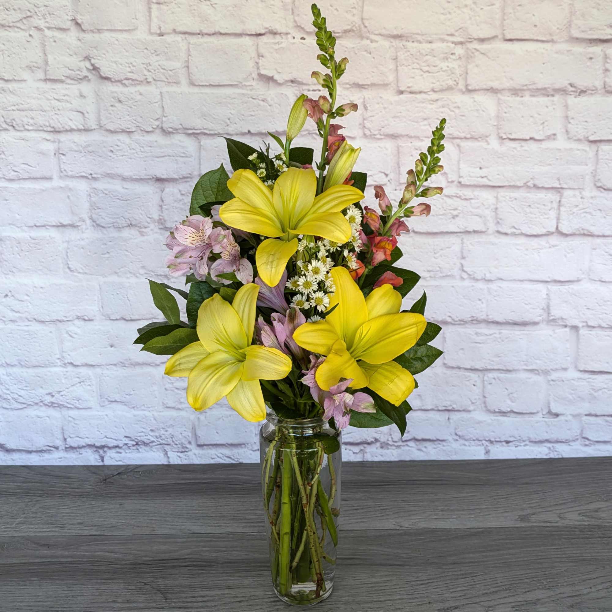 Yellow lilies and pink flowers arranged in a clear glass vase.