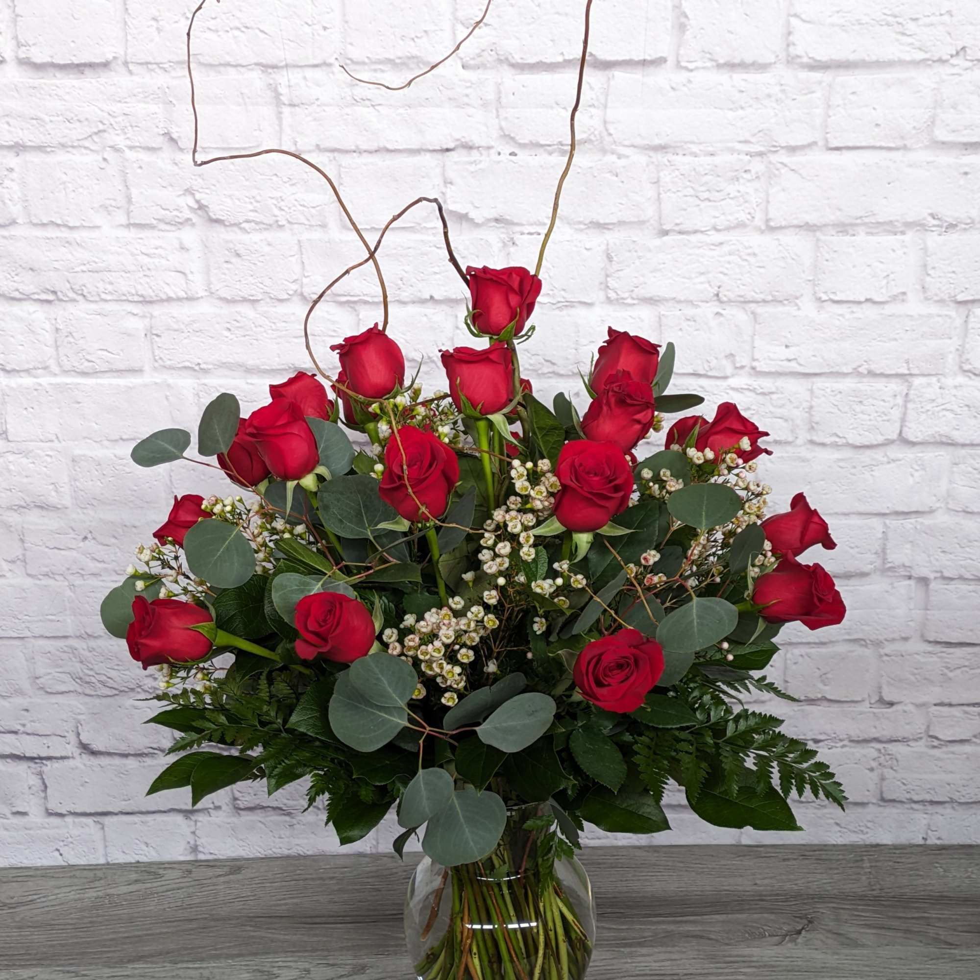 Red roses arranged in a clear glass vase with eucalyptus and white filler flowers