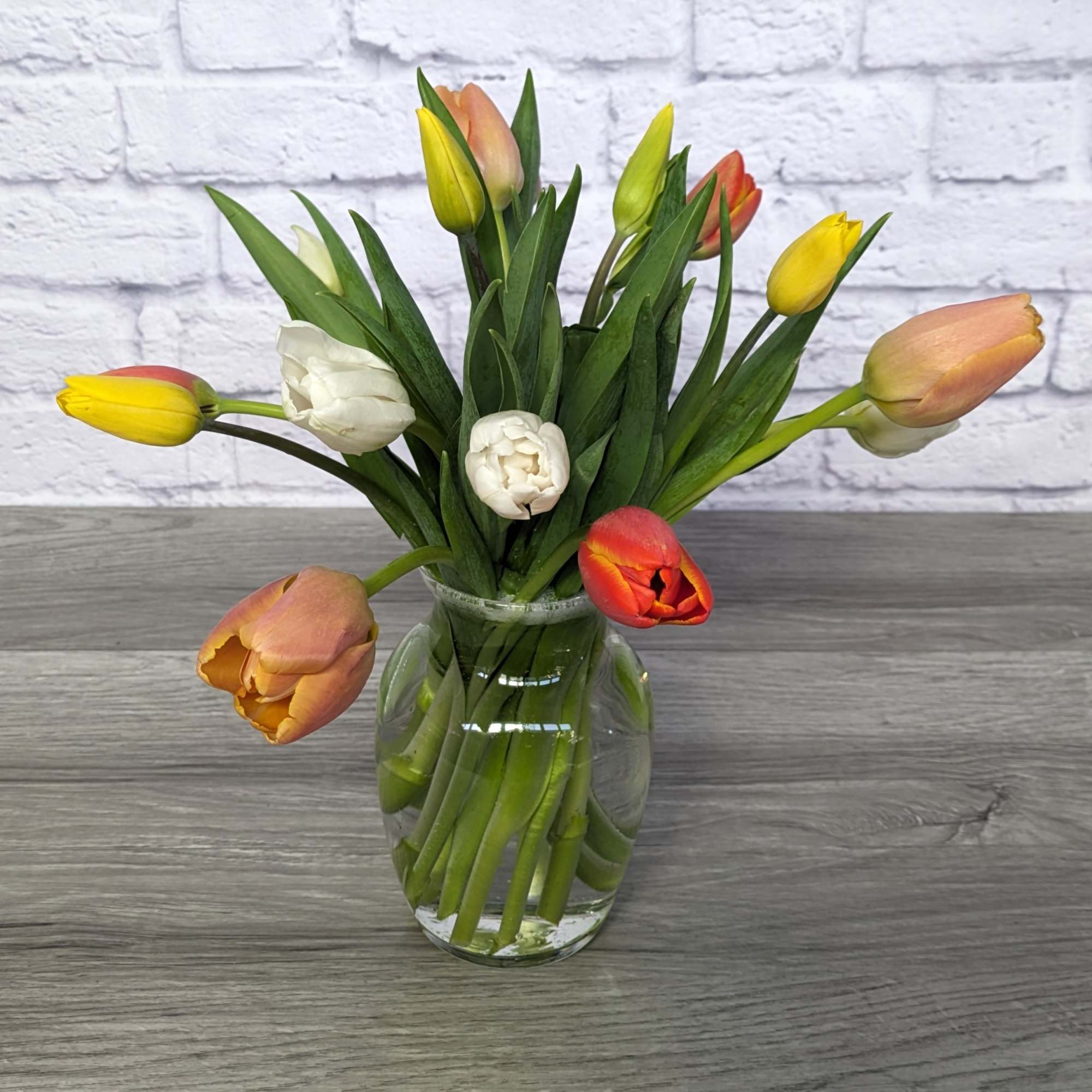 Tulips in yellow, peach, red, and white arranged in a clear glass vase.