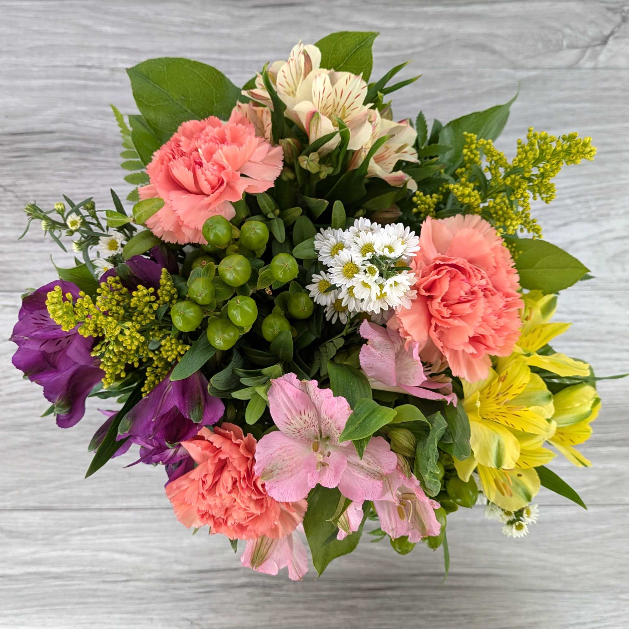 Mixed bouquet with pink carnations, purple and yellow blooms, and white daisies