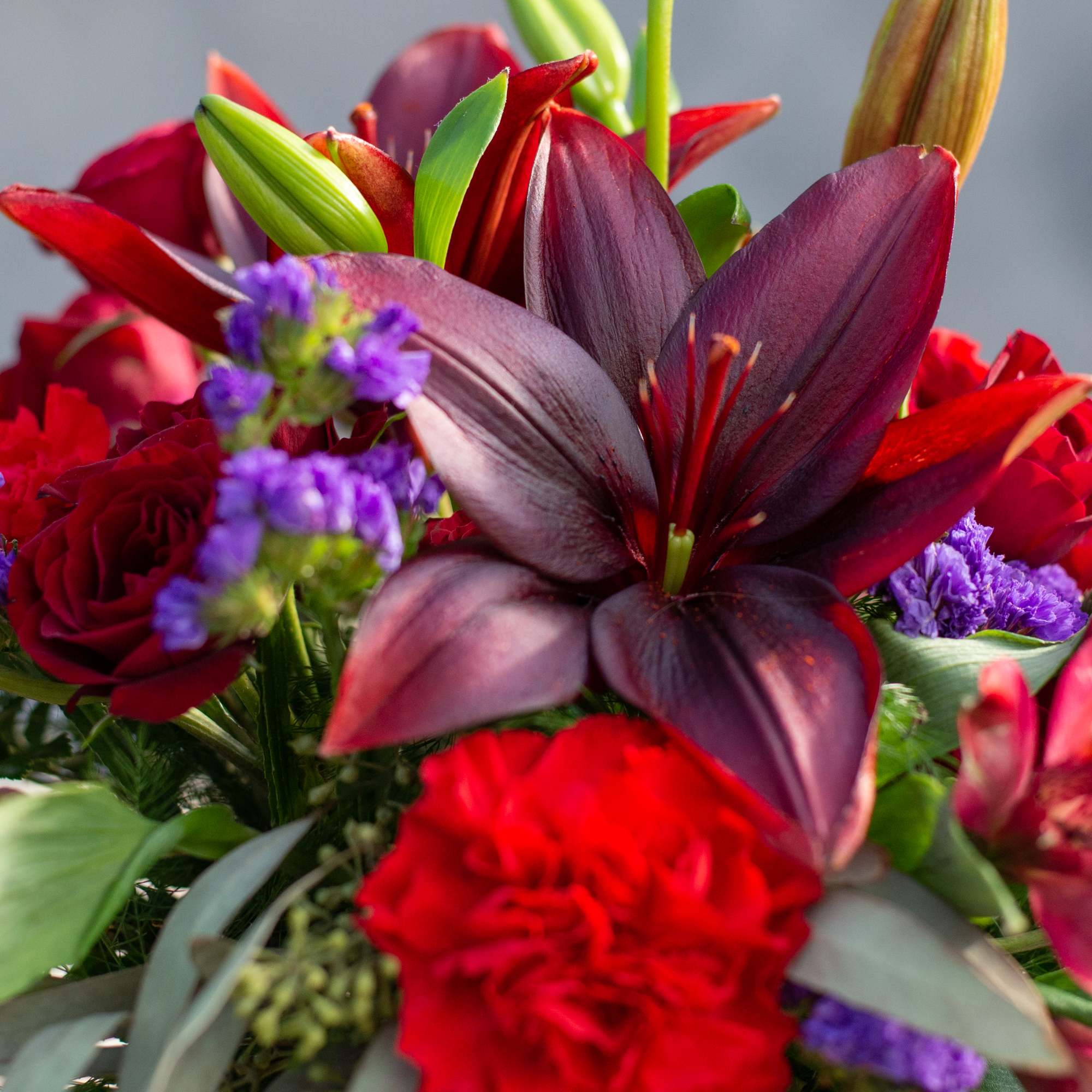 Close-up bouquet of red lilies, roses, and purple filler flowers