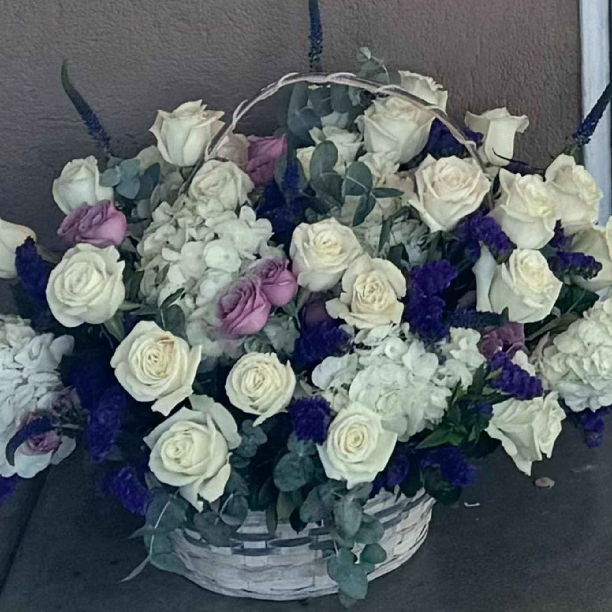 Basket arrangement of white and lavender roses with blue accents