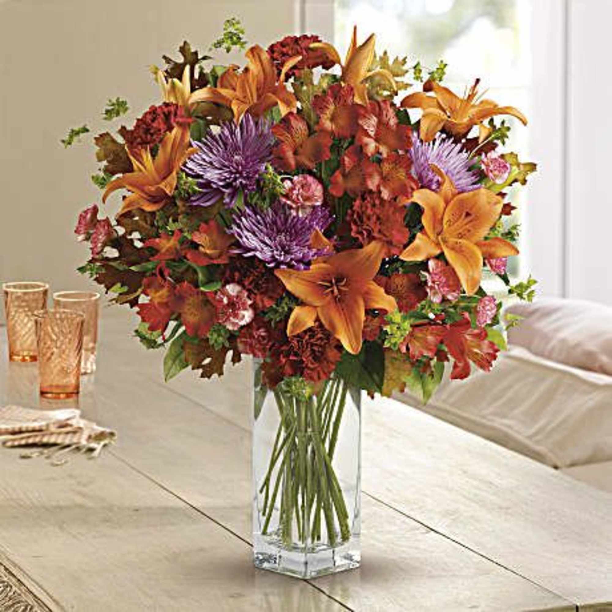 Autumn bouquet of orange lilies and purple chrysanthemums in a clear glass vase