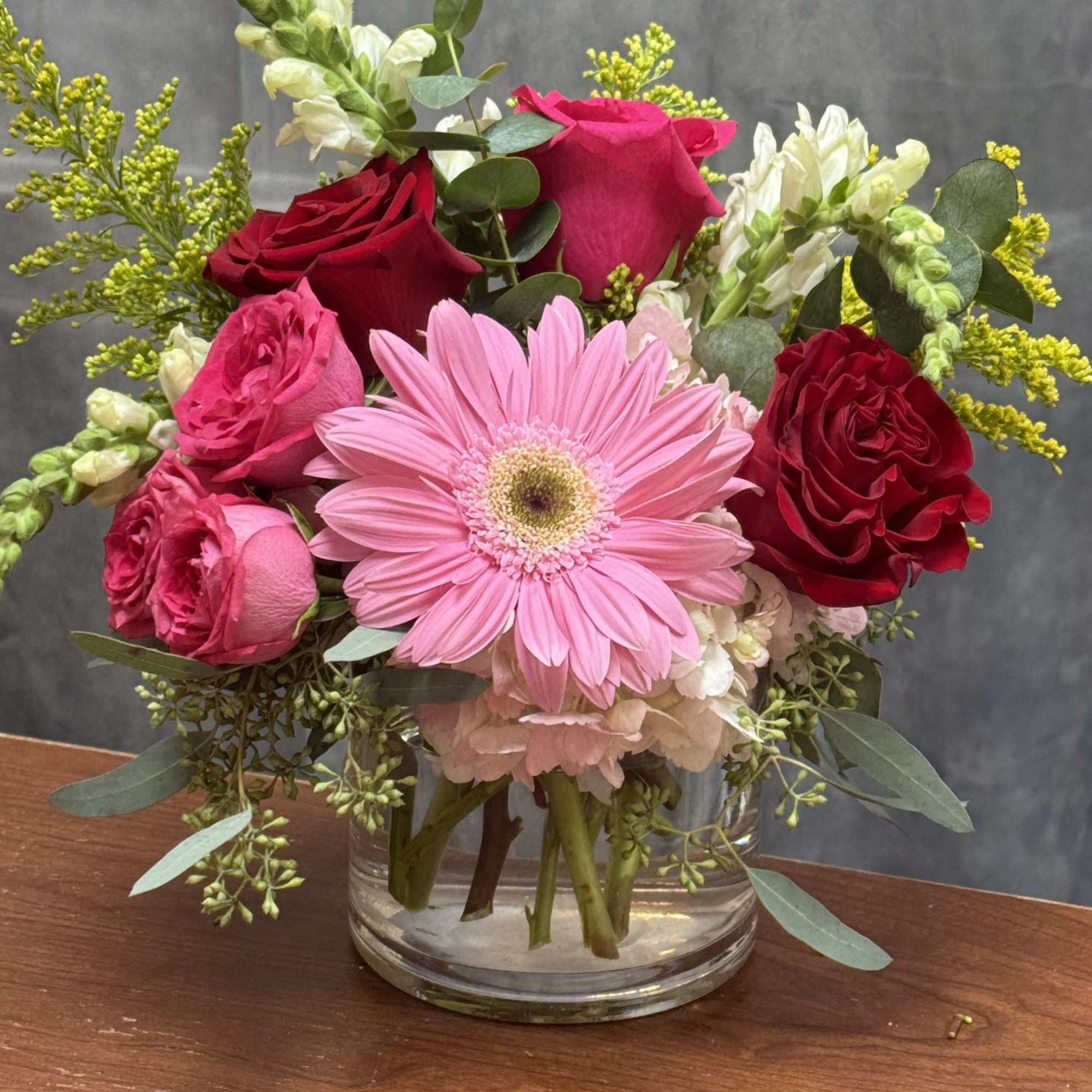 A beautiful mix of red roses, pink gerbera, and seasonal blooms arranged