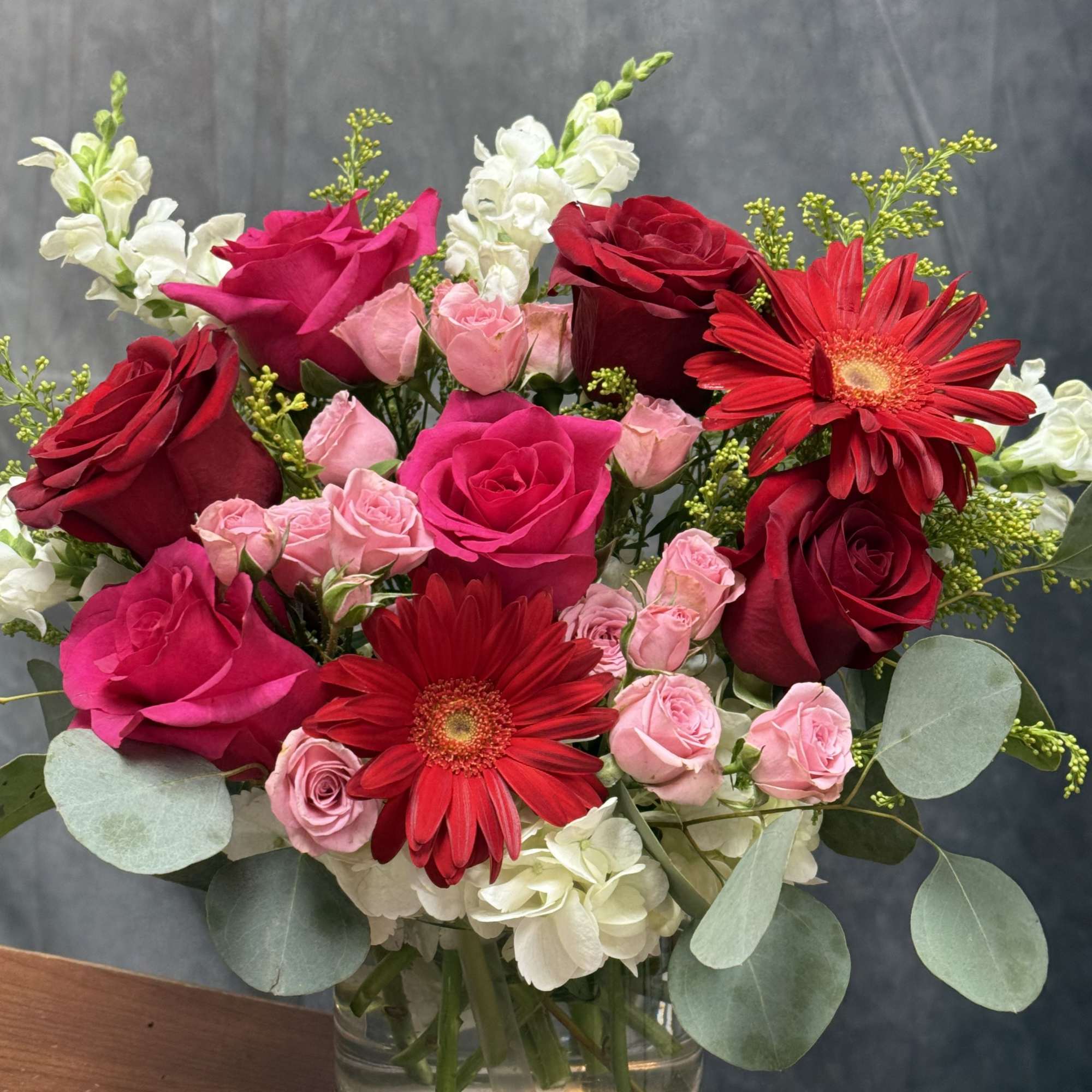 A beautiful mix of red roses, pink gerbera, and seasonal blooms arranged