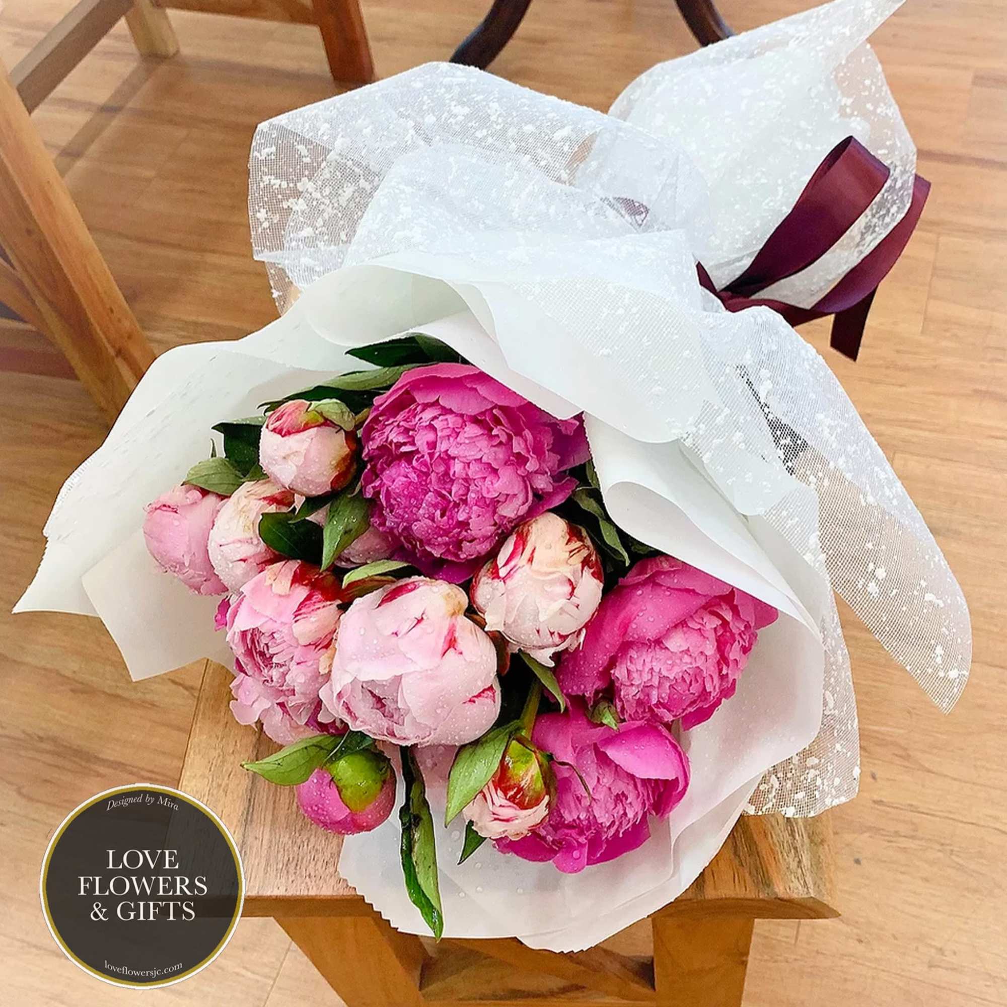 Hand-tied bouquet of pink peony blooms wrapped in white paper with dotted mesh and ribbon