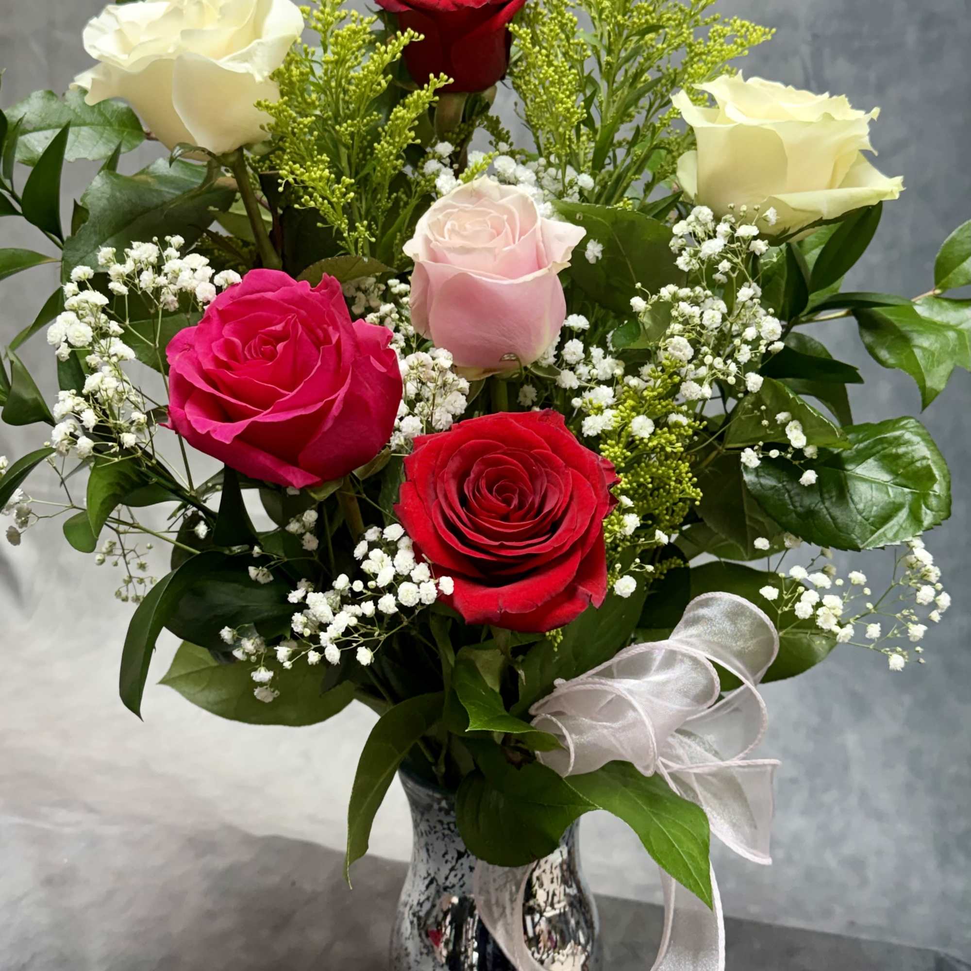 Bouquet of red, pink, and white roses in a silver vase with a ribbon