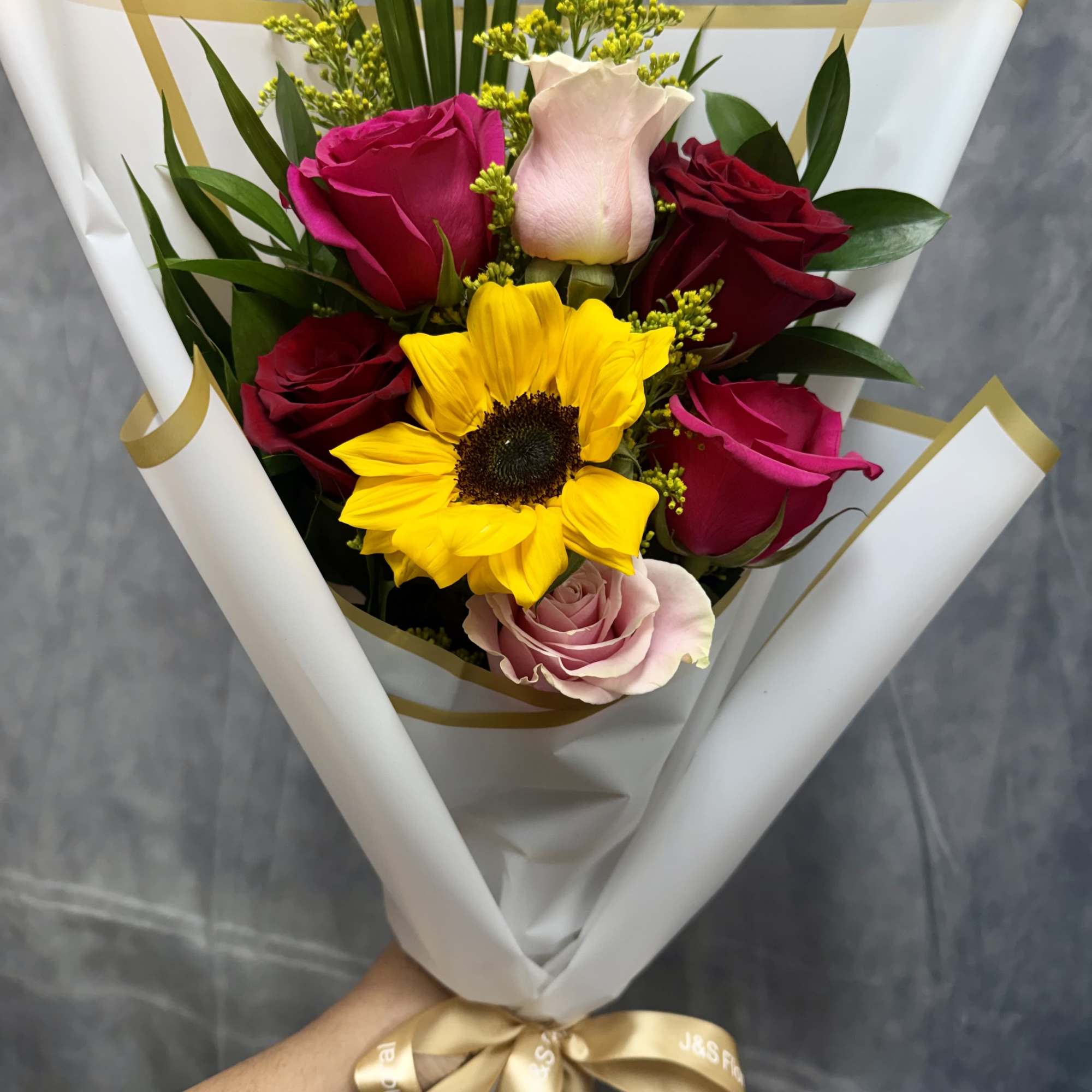 Bouquet of roses and a sunflower wrapped in white paper with a gold ribbon