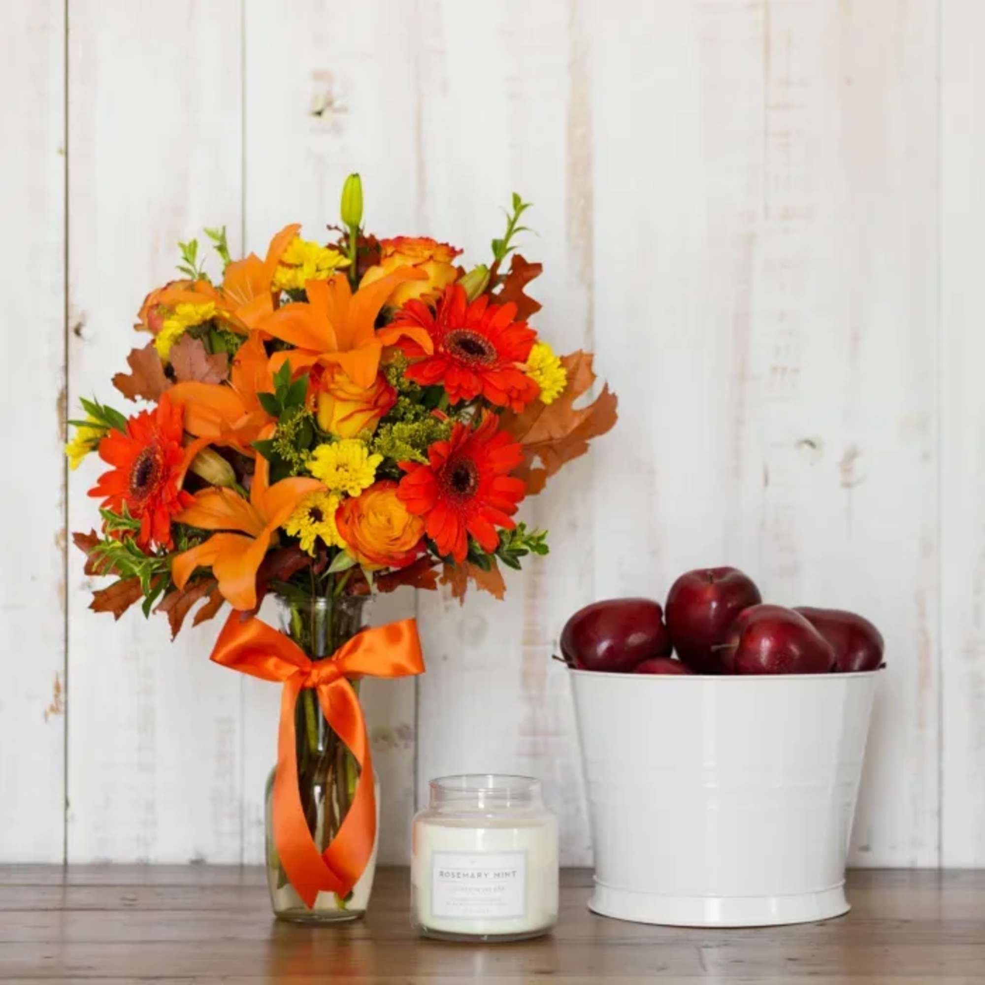Orange and red mixed bouquet in a glass vase with an orange ribbon.