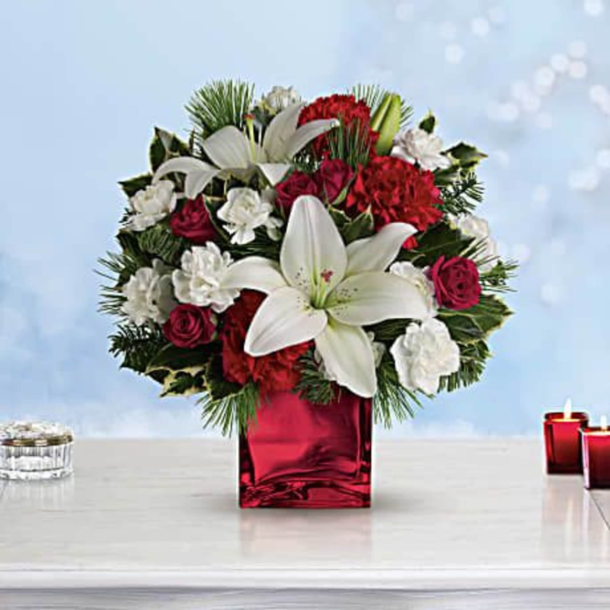 Red and white floral arrangement in a red glass vase with candles nearby