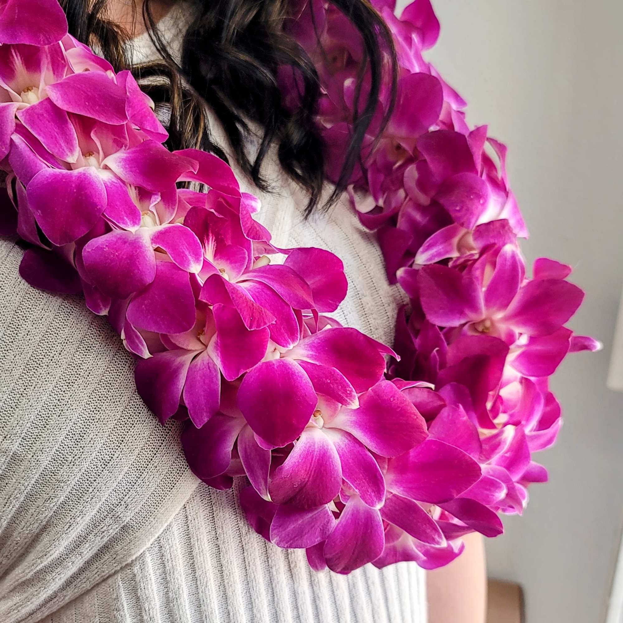 Woman wearing a bright pink orchid lei over a light sweater
