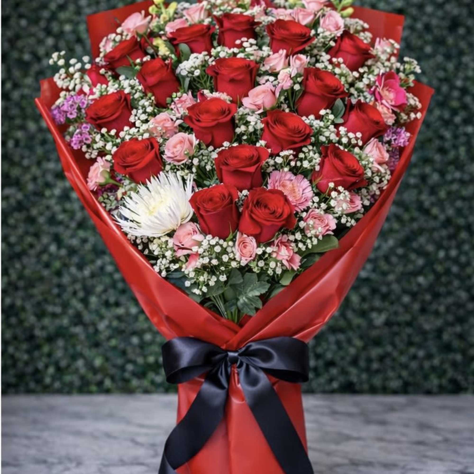 Bouquet of red and pink roses wrapped in red paper with a black ribbon