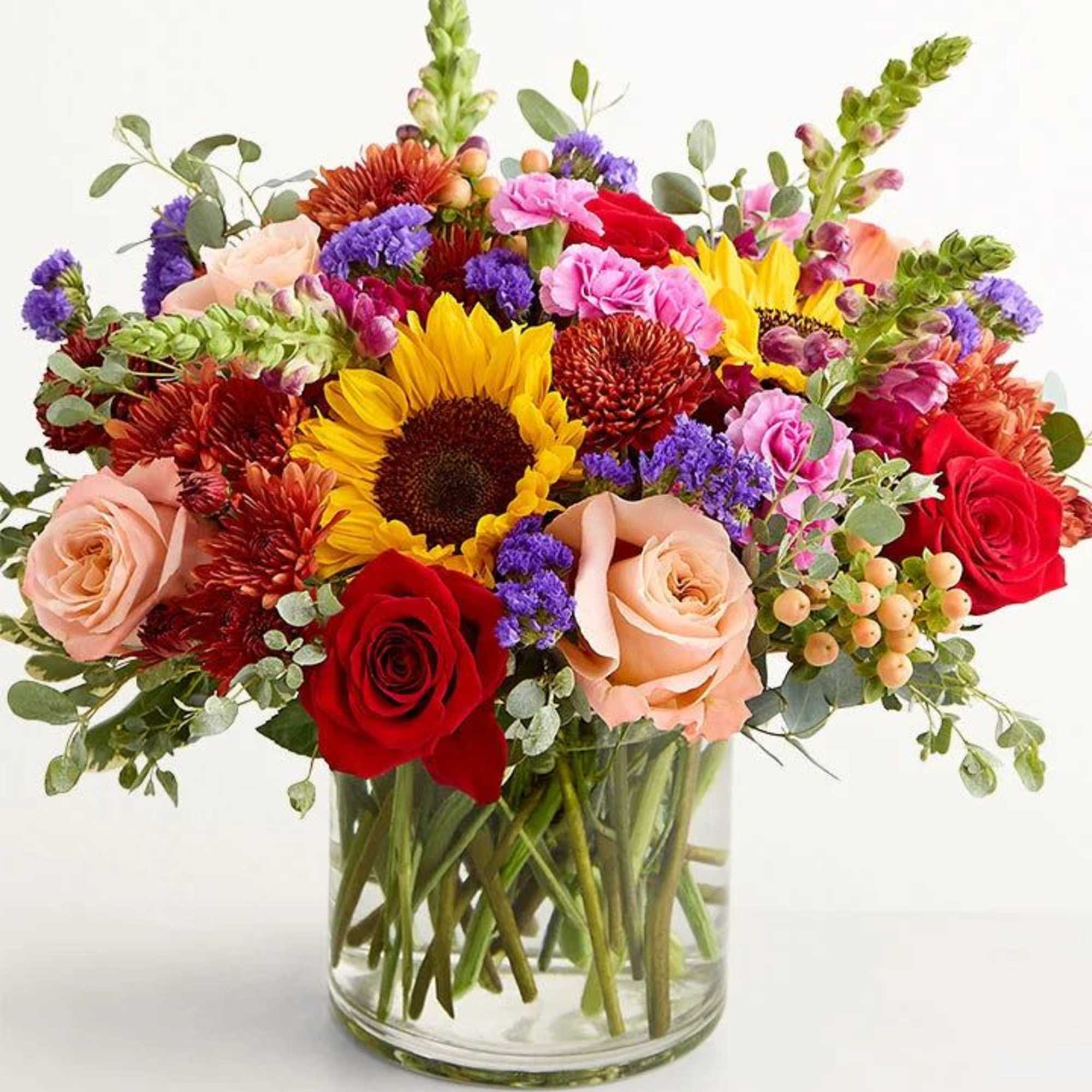 Mixed bouquet of roses, sunflowers, and chrysanthemums in a glass vase