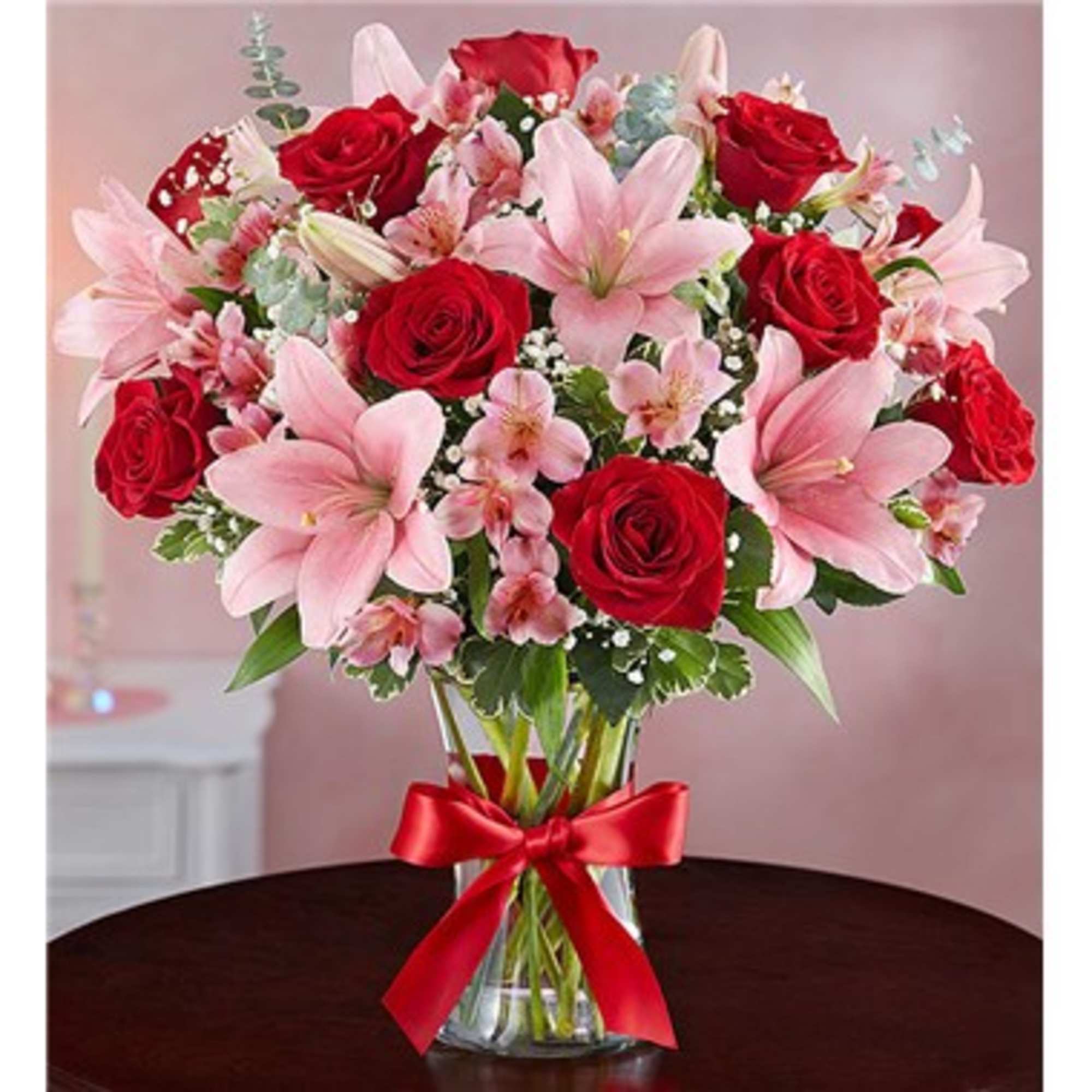 Bouquet of pink lilies and red roses in a glass vase with a red ribbon