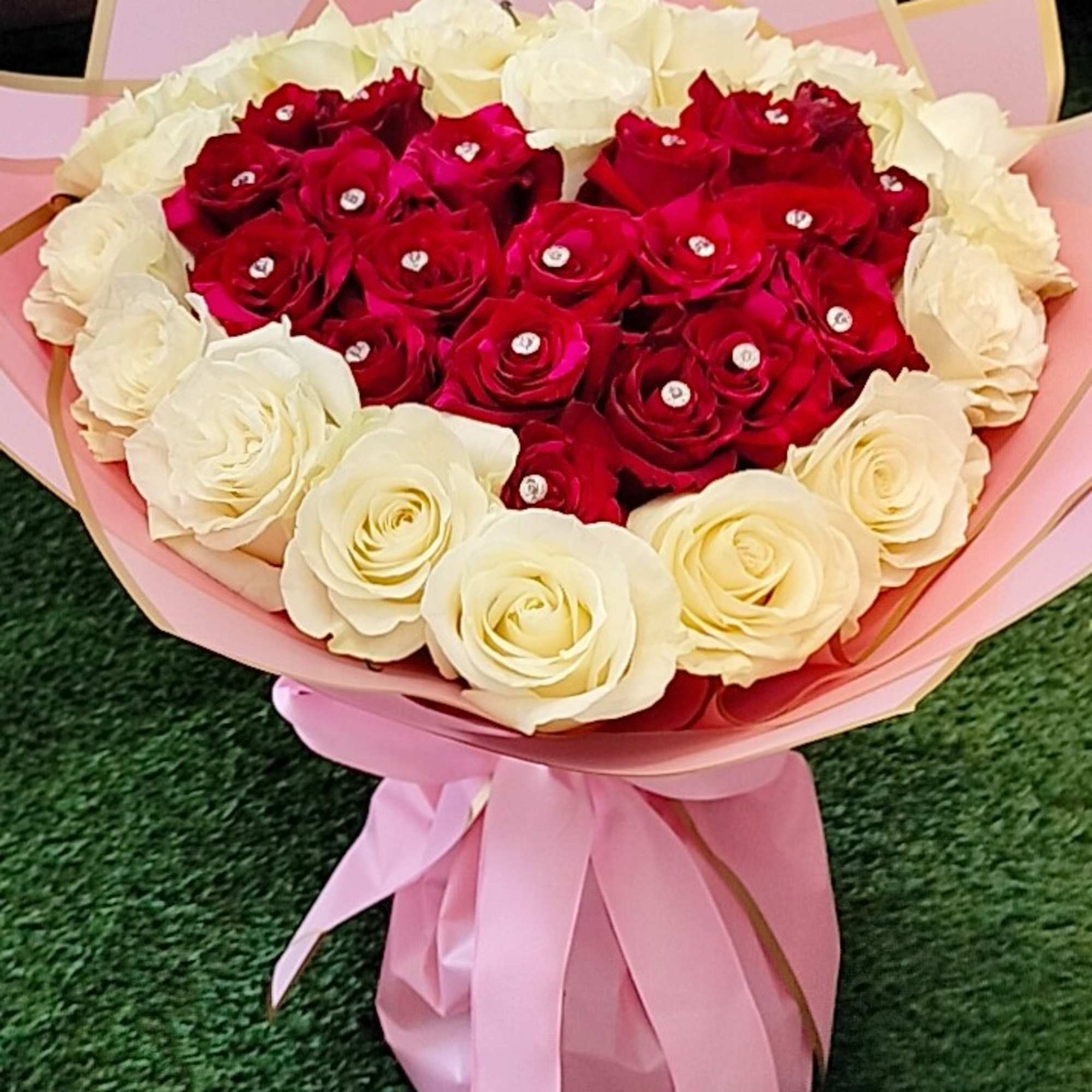Heart-shaped bouquet of red and white roses wrapped in pink paper