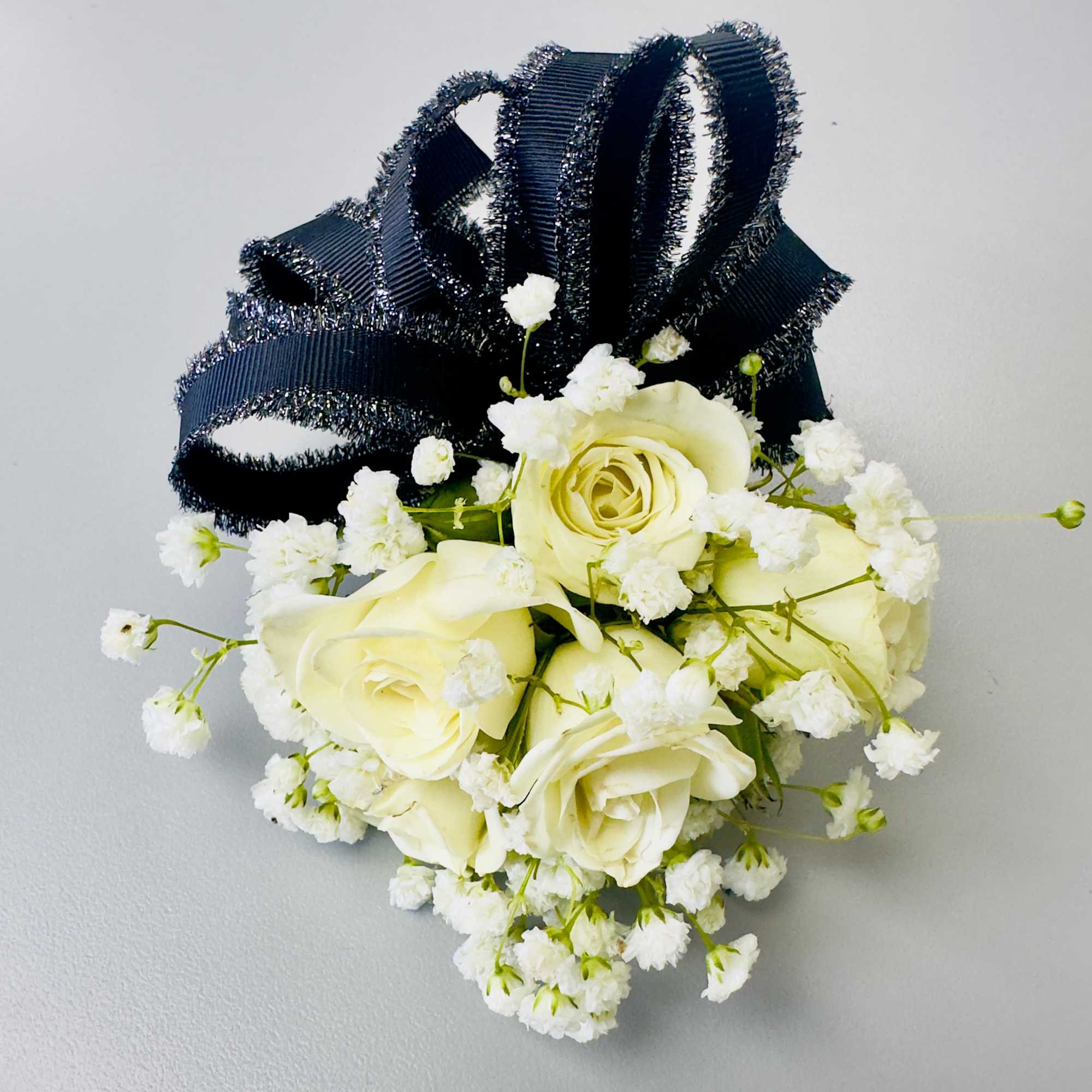 Creamy white roses clustered into a compact, hand-tied corsage give this wrist