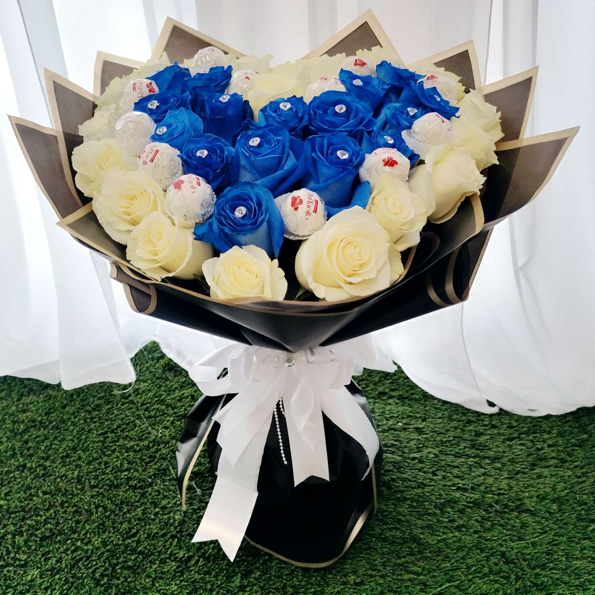 Bouquet of blue and white roses wrapped in black paper with a white ribbon