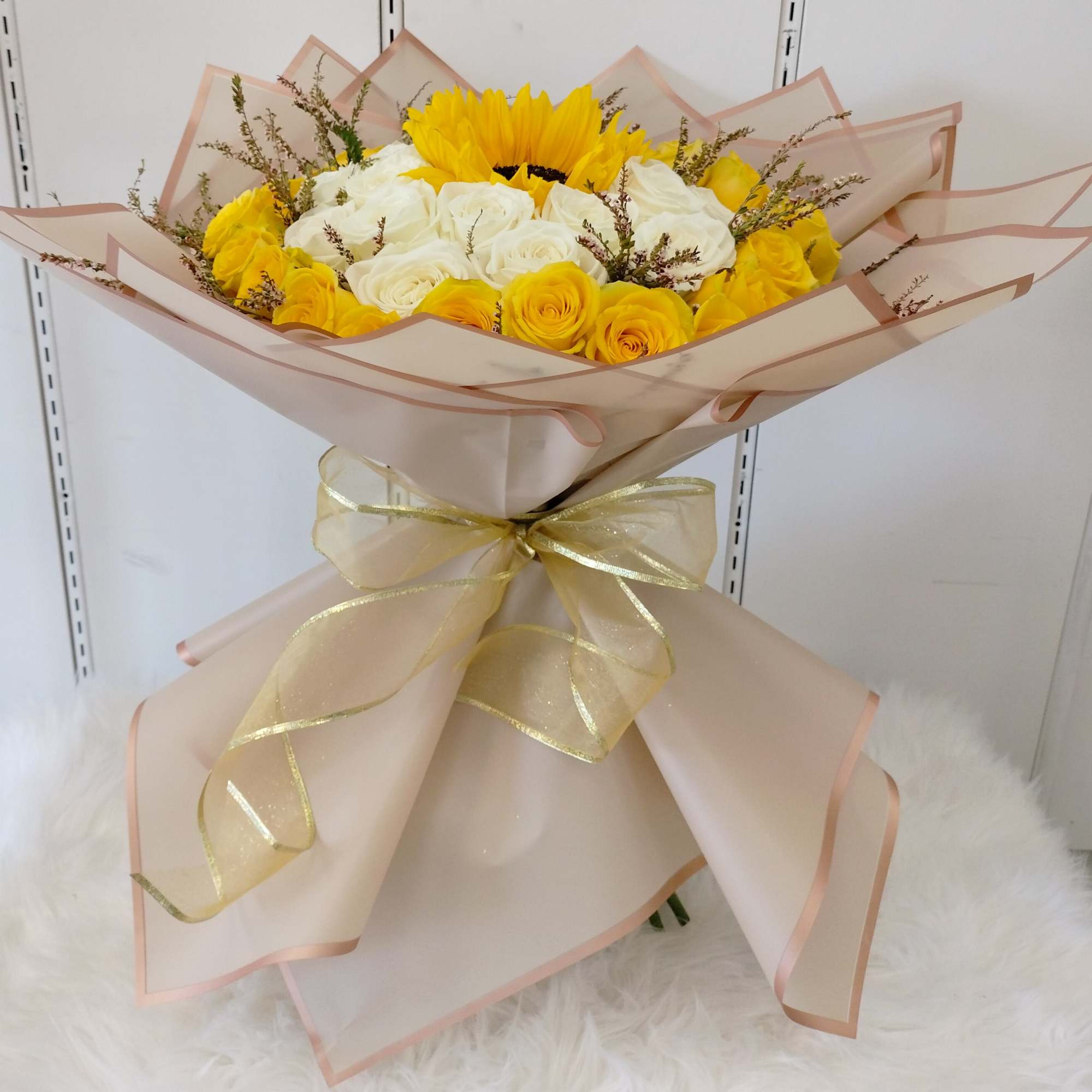 Bouquet of yellow and white roses wrapped in pale pink paper with a gold ribbon