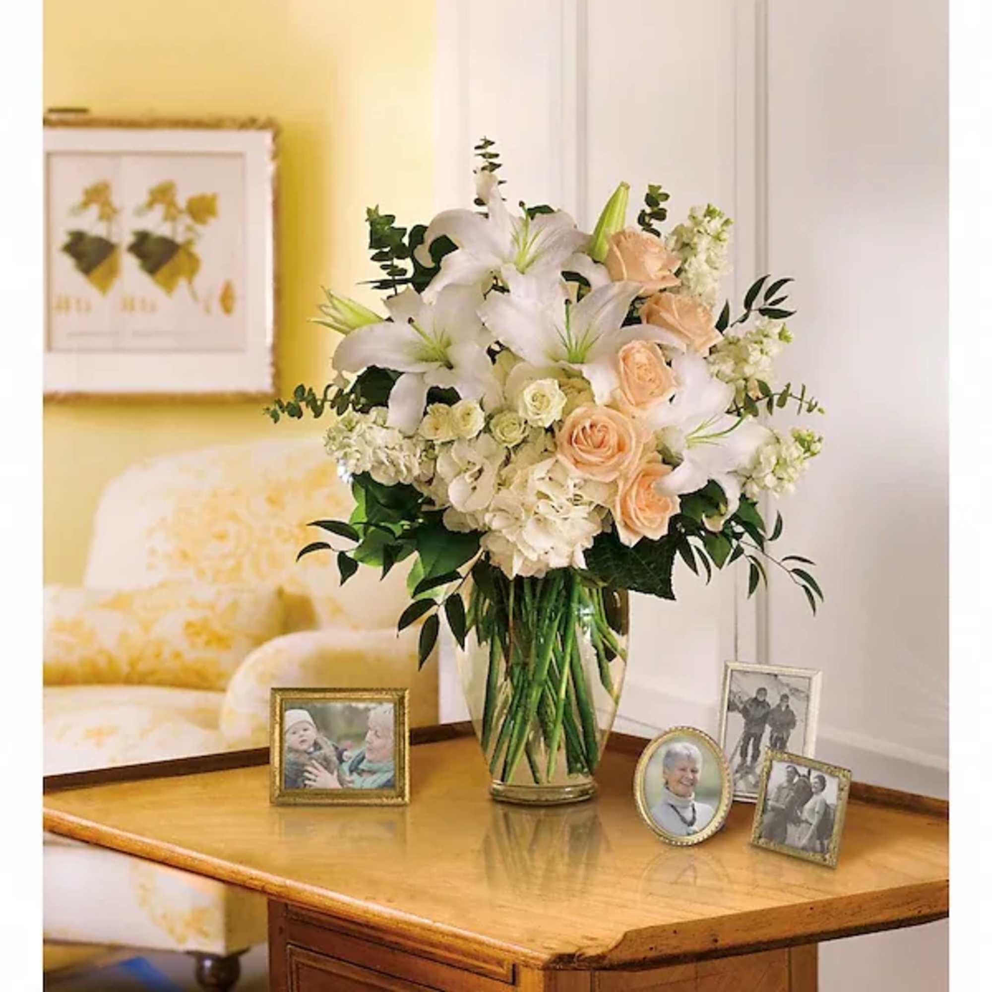 White lilies and peach roses arranged in a glass vase on a table