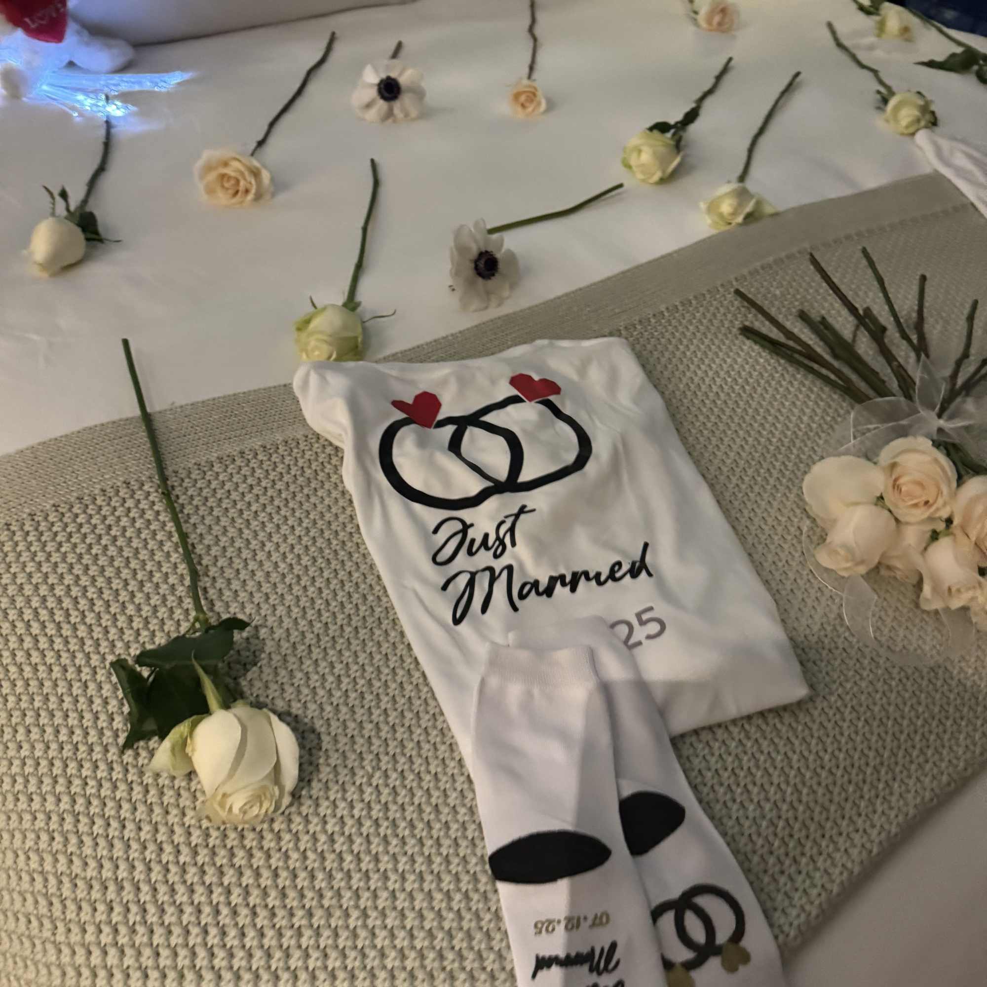 White roses and small daisies arranged around a "Just Married" outfit display.