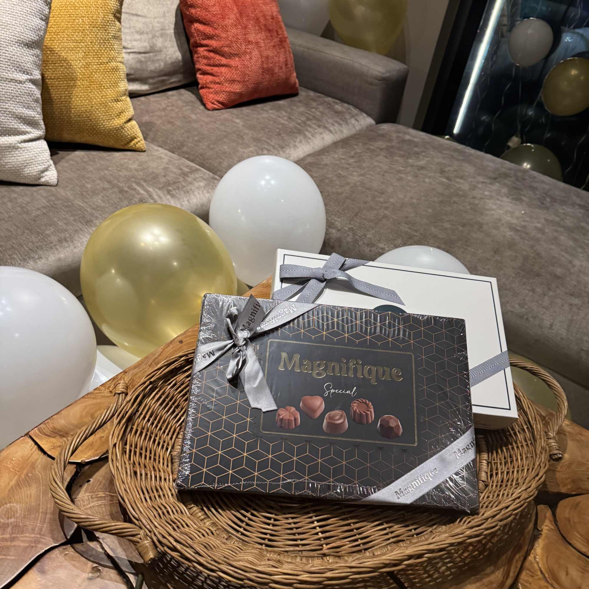 Gift basket with chocolate boxes and balloons on a couch