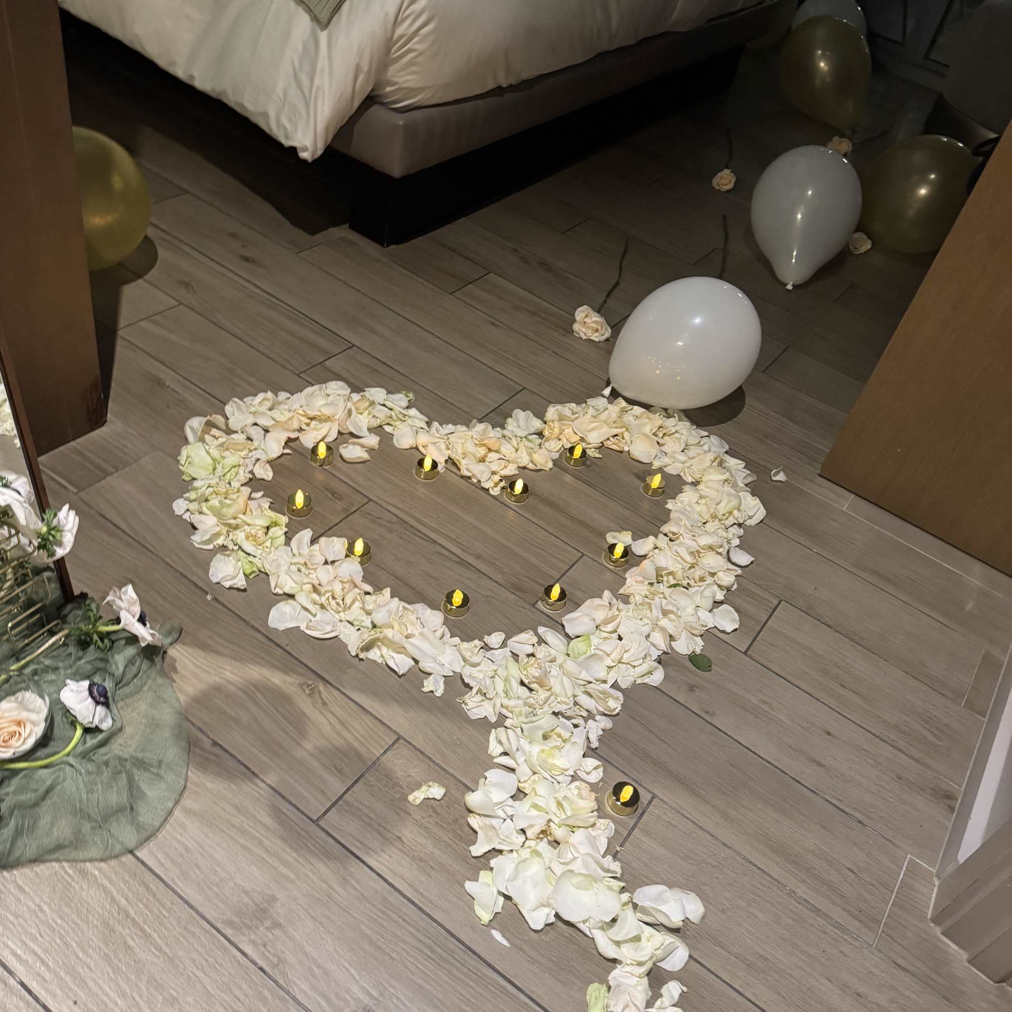 Heart-shaped flower petal arrangement on the floor with small candles and balloons