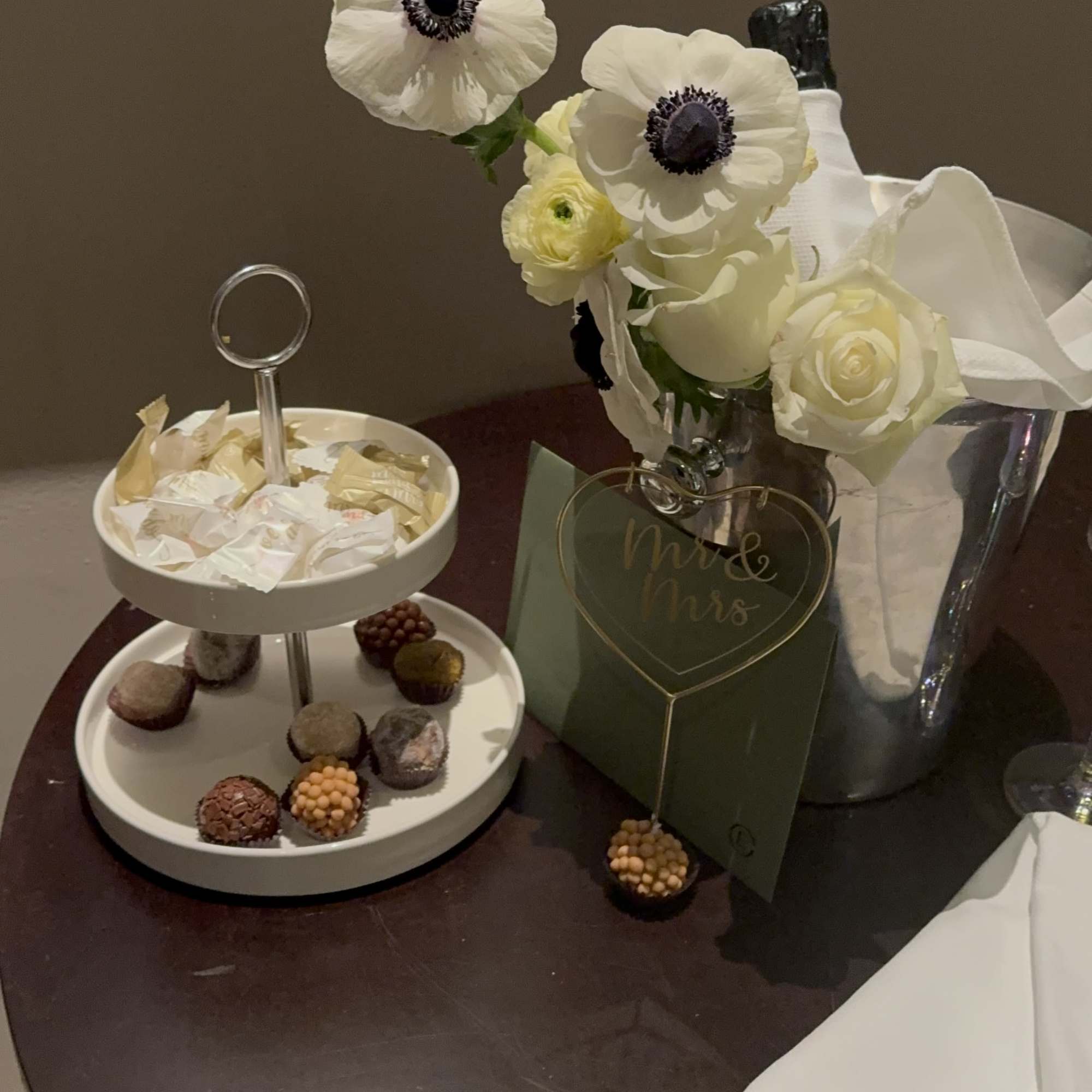 White flowers in a clear vase beside a tiered tray of chocolates